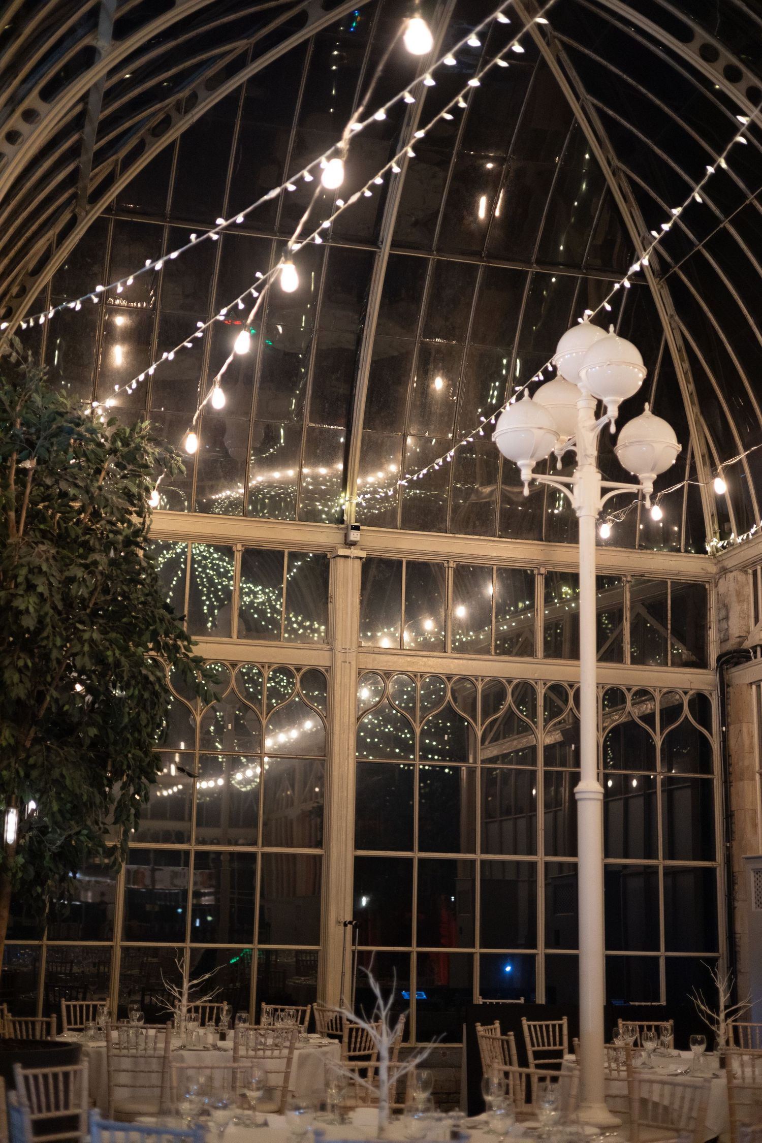 Glass conservatory ceiling with string lights creating a romantic evening atmosphere.
