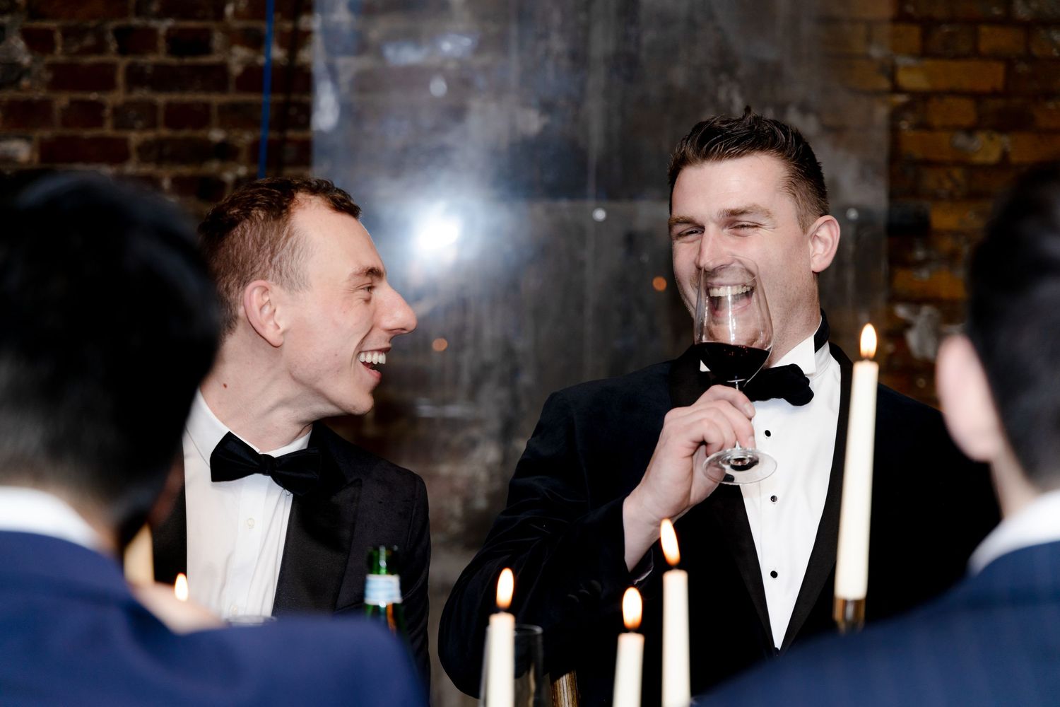 Two people in formal attire sharing a laugh at an elegant candlelit dinner setting.
