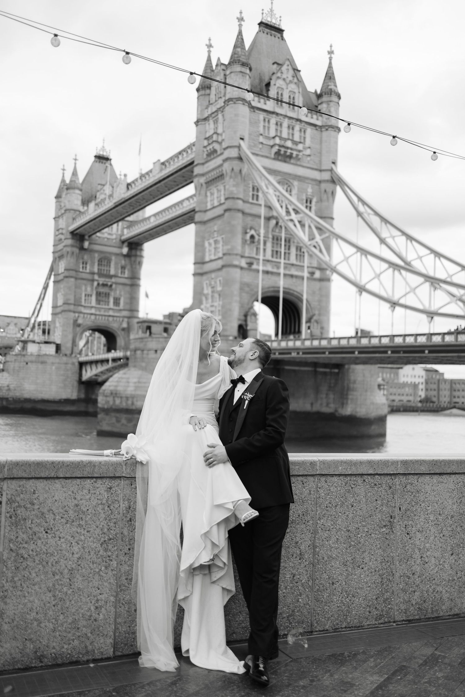 Black and white wedding portrait with Tower Bridge creating dramatic London backdrop.