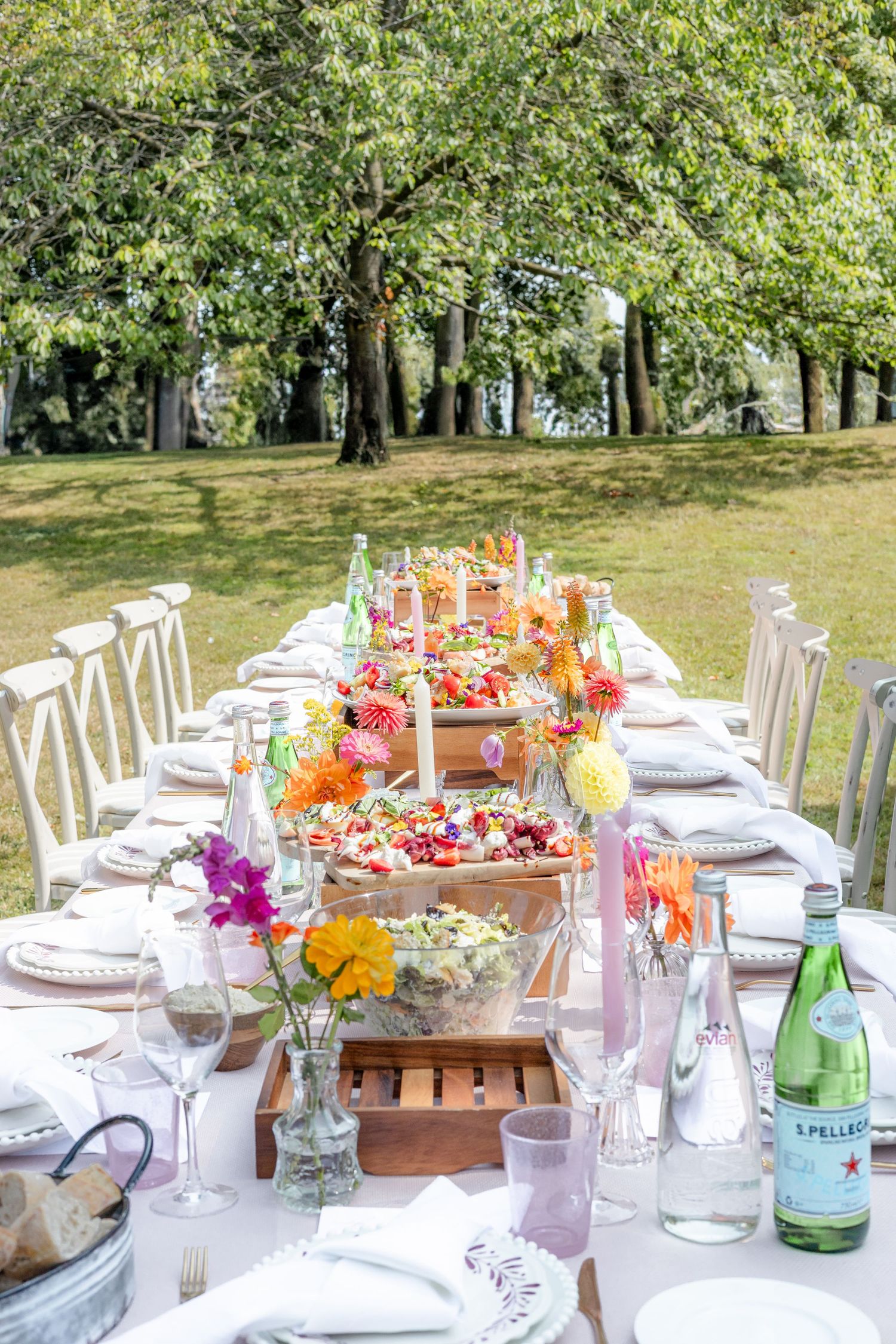 Long banquet table decorated with vibrant floral arrangements and place settings in an outdoor garden.