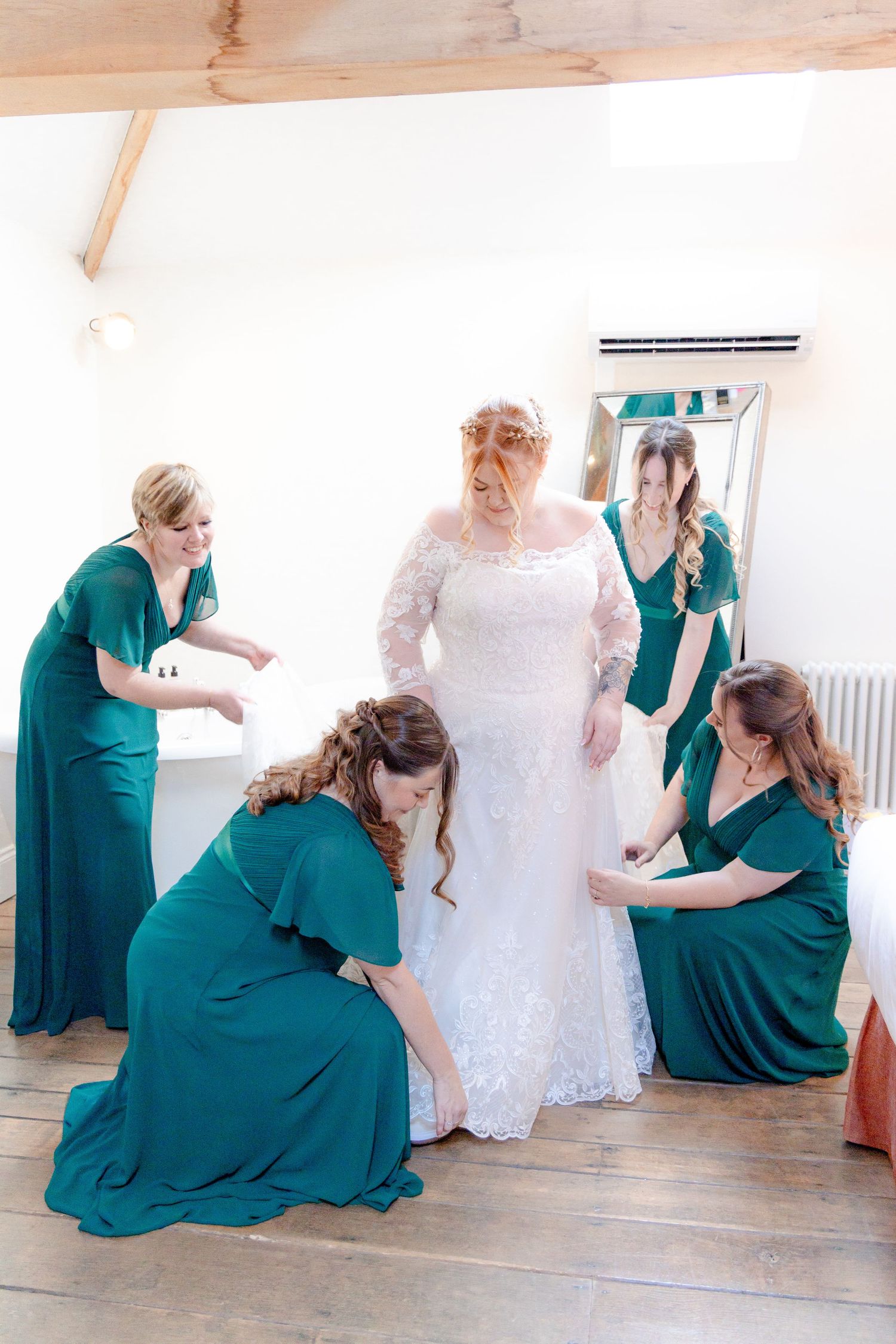 Bridesmaids in teal dresses help adjust bride's wedding gown during preparation.