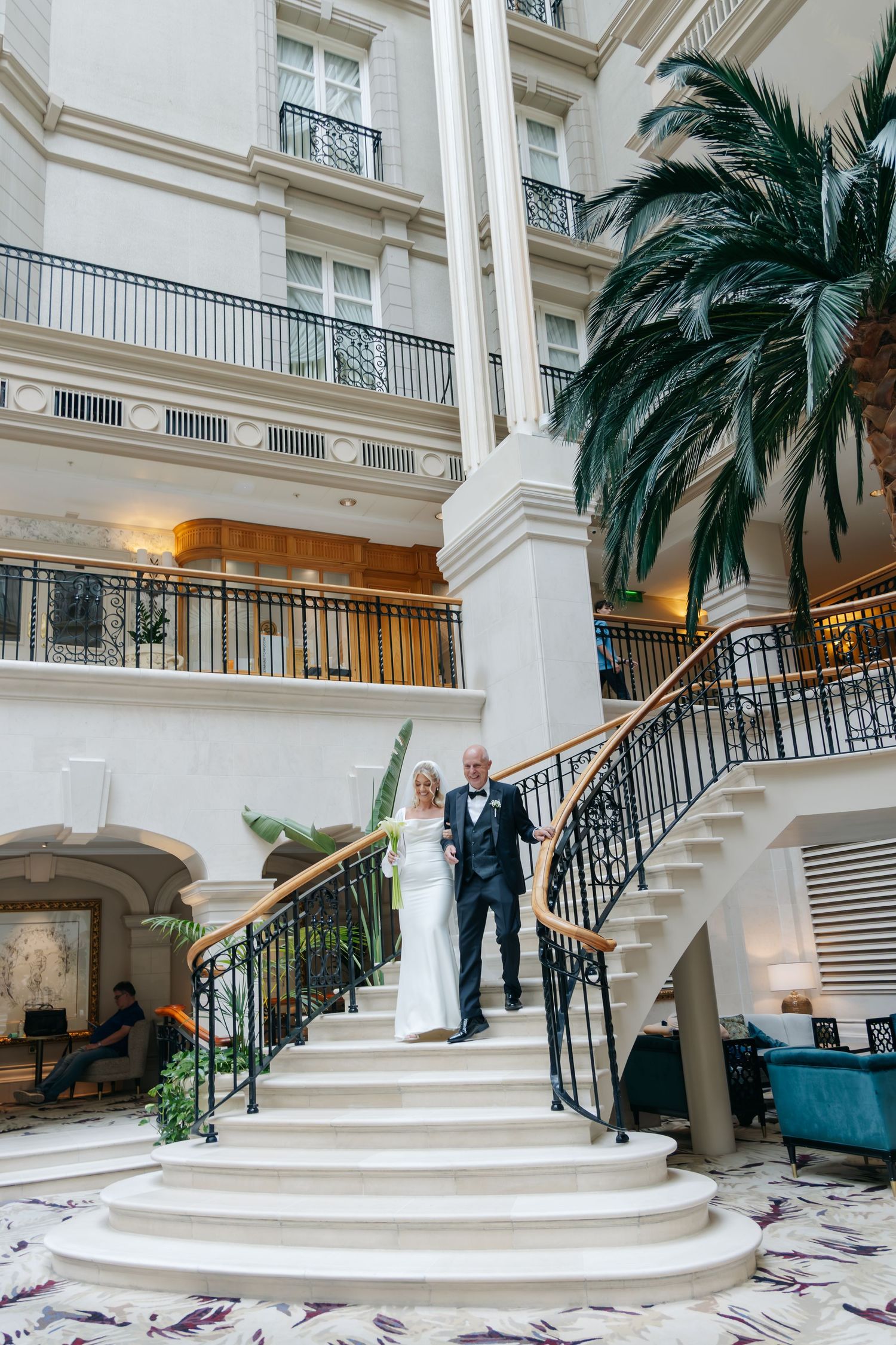 Elegant wedding couple descending grand white marble staircase in luxurious venue.