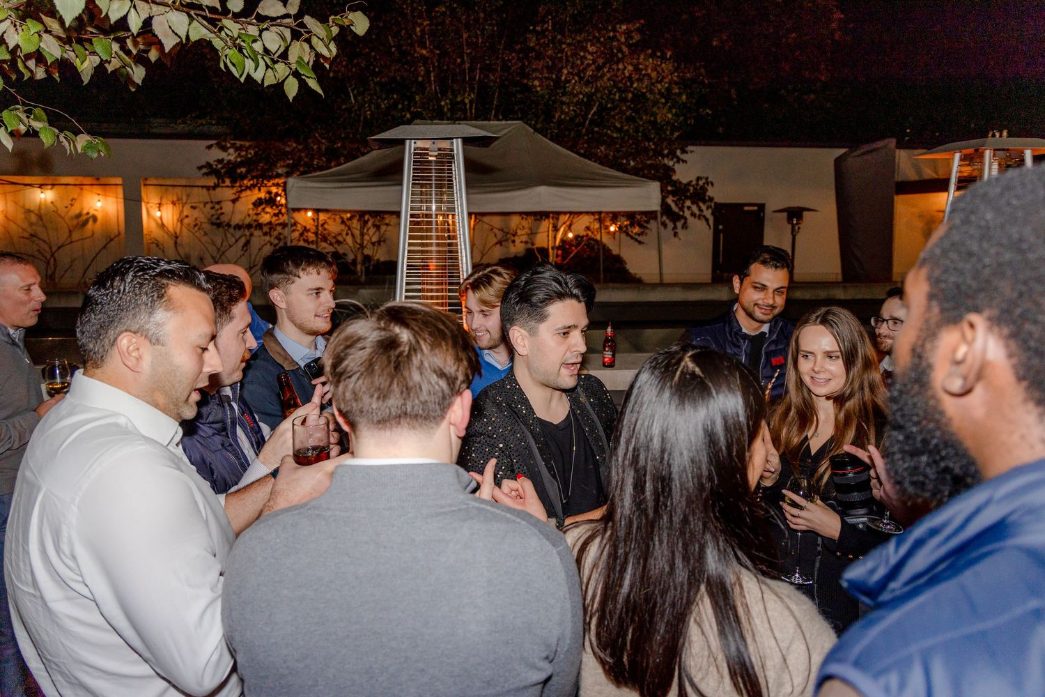A crowd of people gathered outdoors at night having animated conversations.