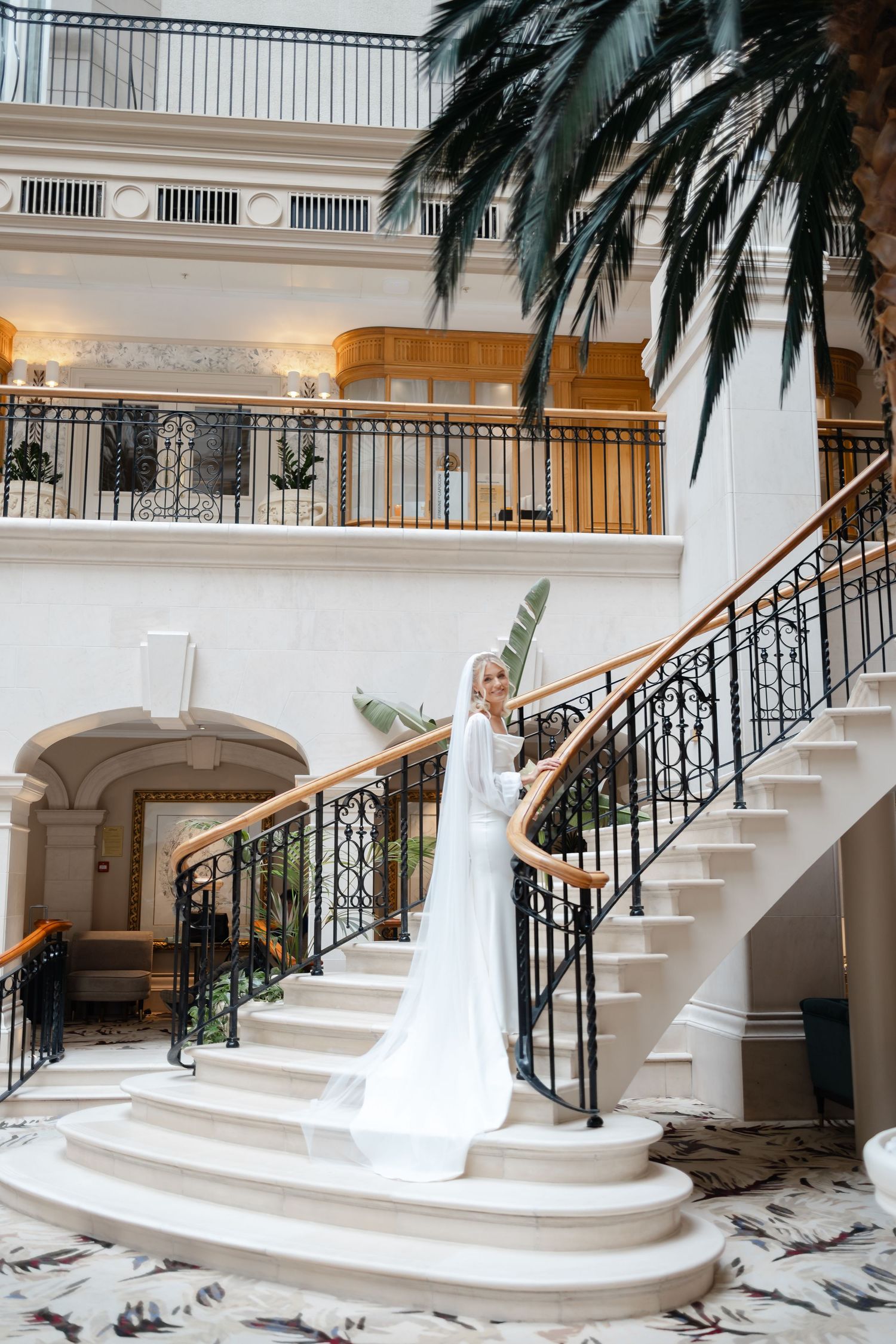 Elegant white staircase with palm trees and black railings in upscale venue.