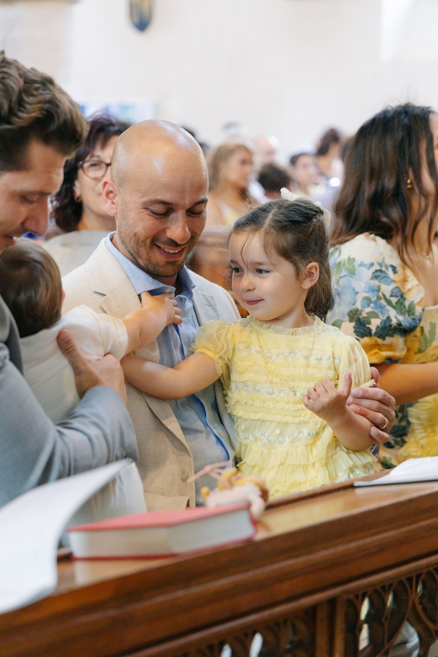 Child in yellow dress sitting with family during church service.