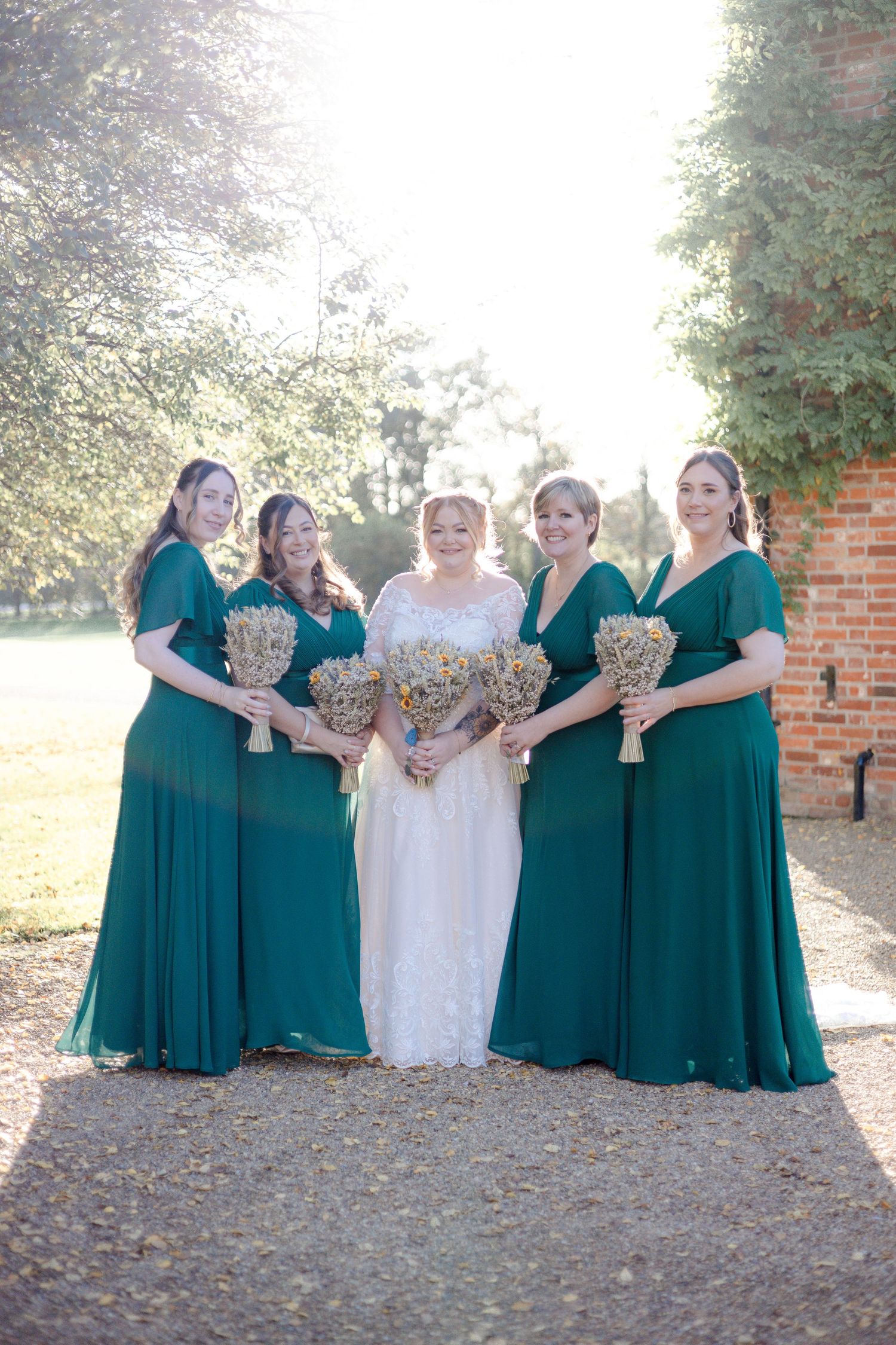 Bridal party in emerald green dresses poses outdoors on autumn day.
