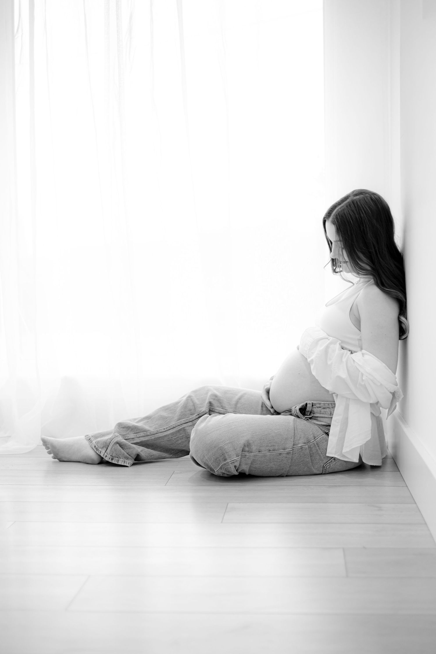 Artistic maternity portrait of expectant mother sitting by window in natural light.