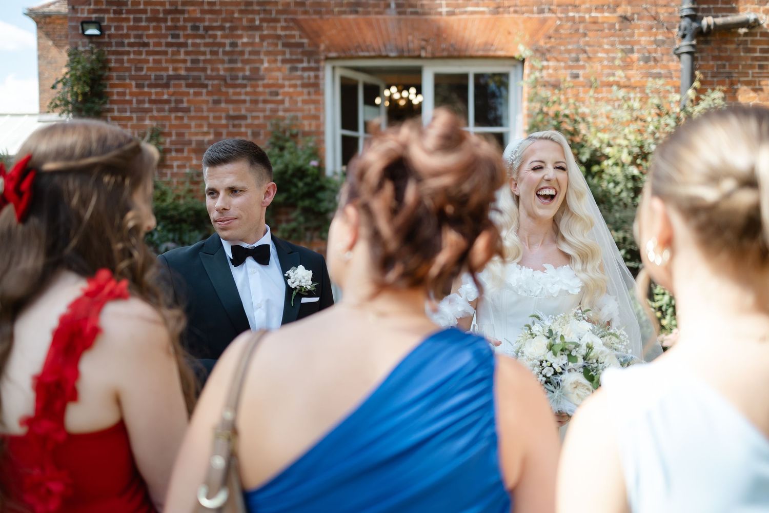 Candid wedding party photo with guests in formal attire against brick wall backdrop.