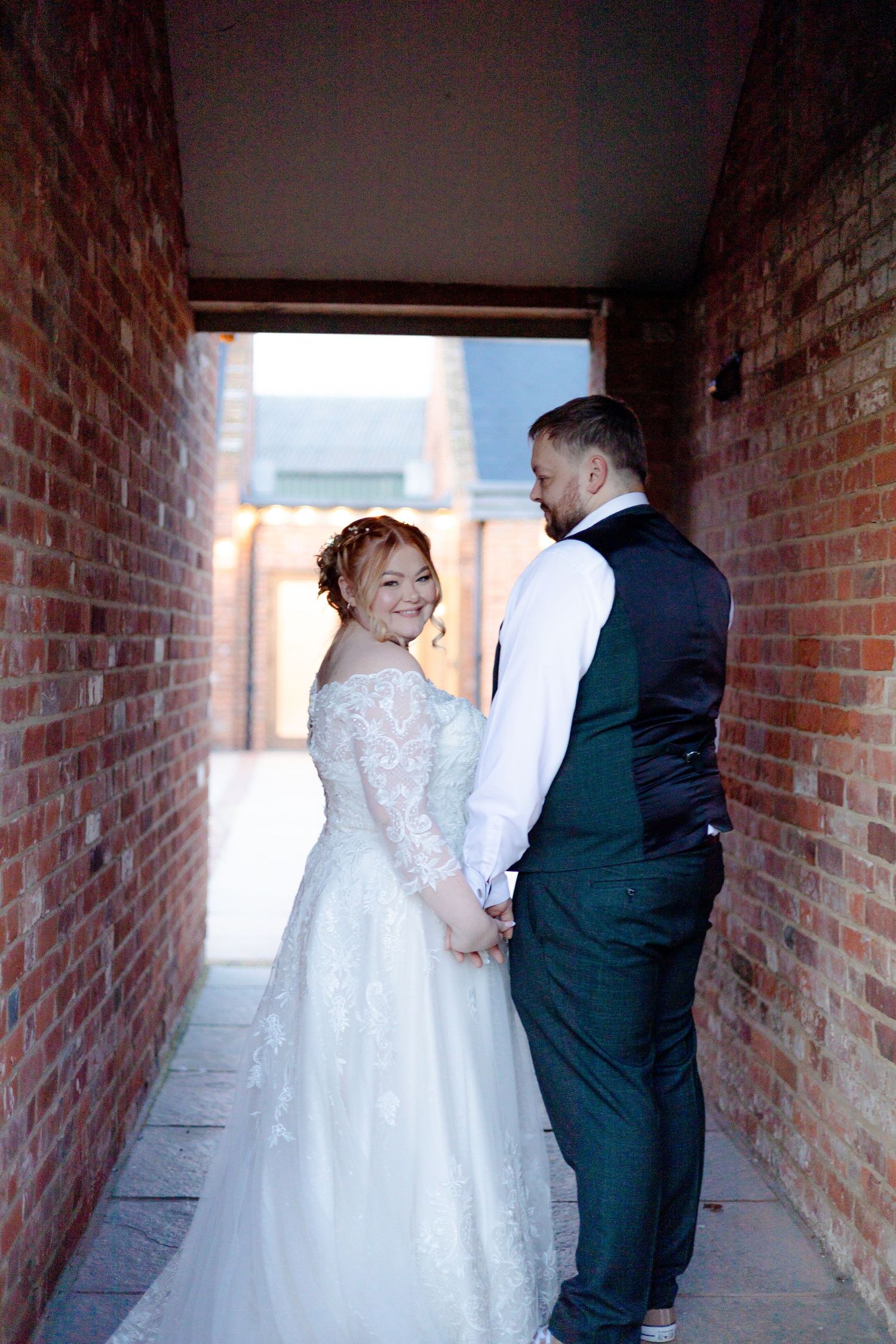 Wedding couple shares intimate moment in brick passageway.