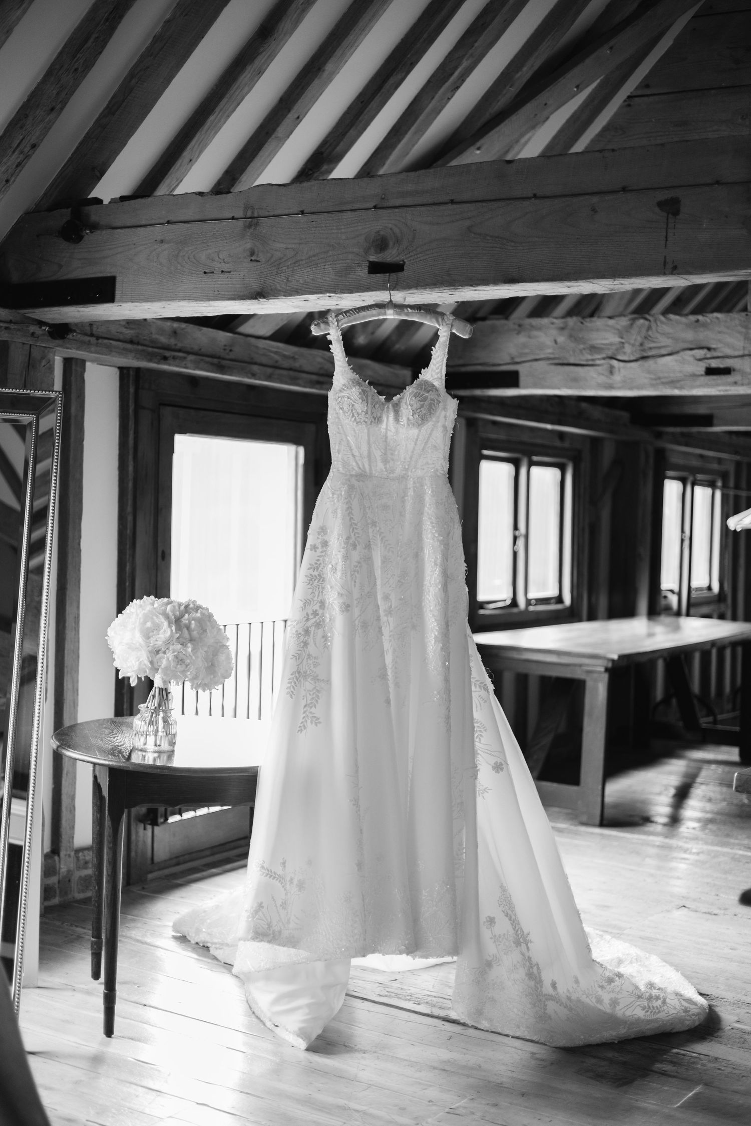 Collection of white wedding dresses hanging in rustic wooden attic space.