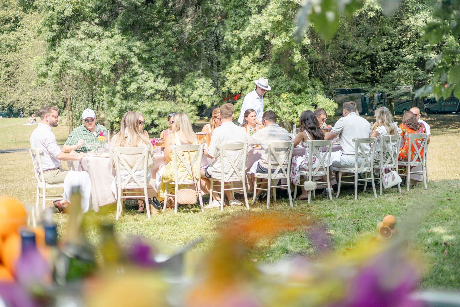 Outdoor garden party dining setup with white chairs and colorful flowers in the foreground.