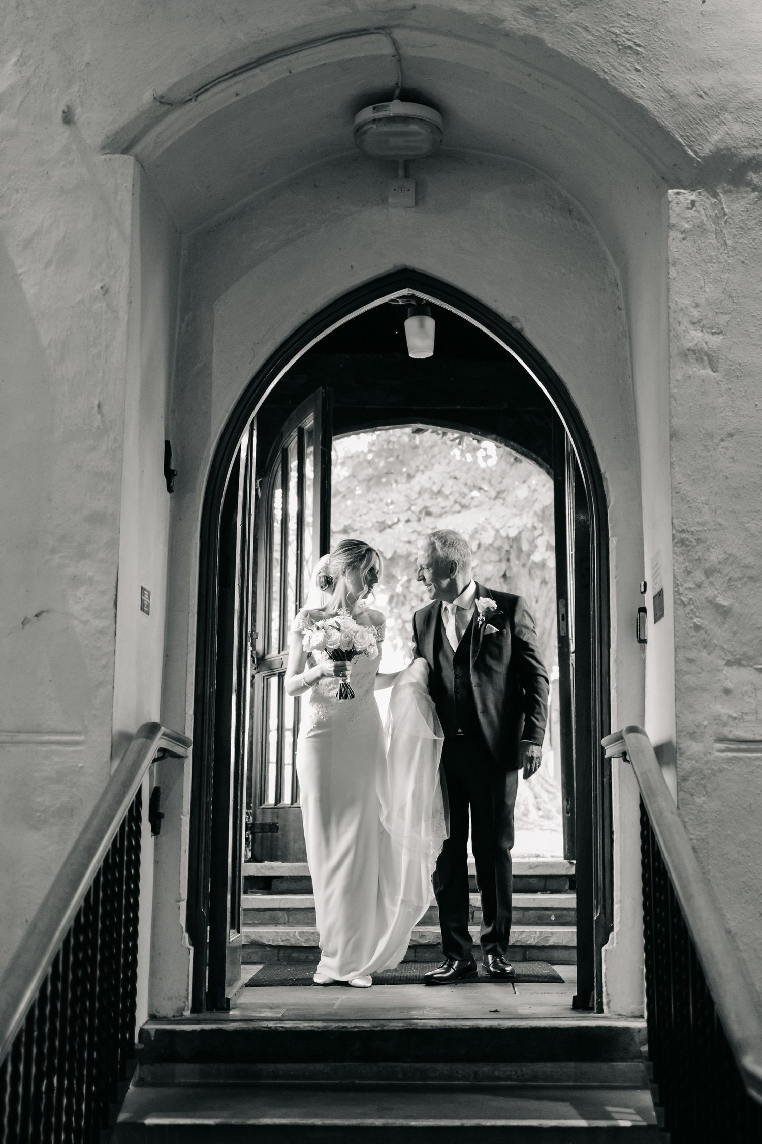 Dramatic black and white photos through stone archway during wedding ceremony processional.