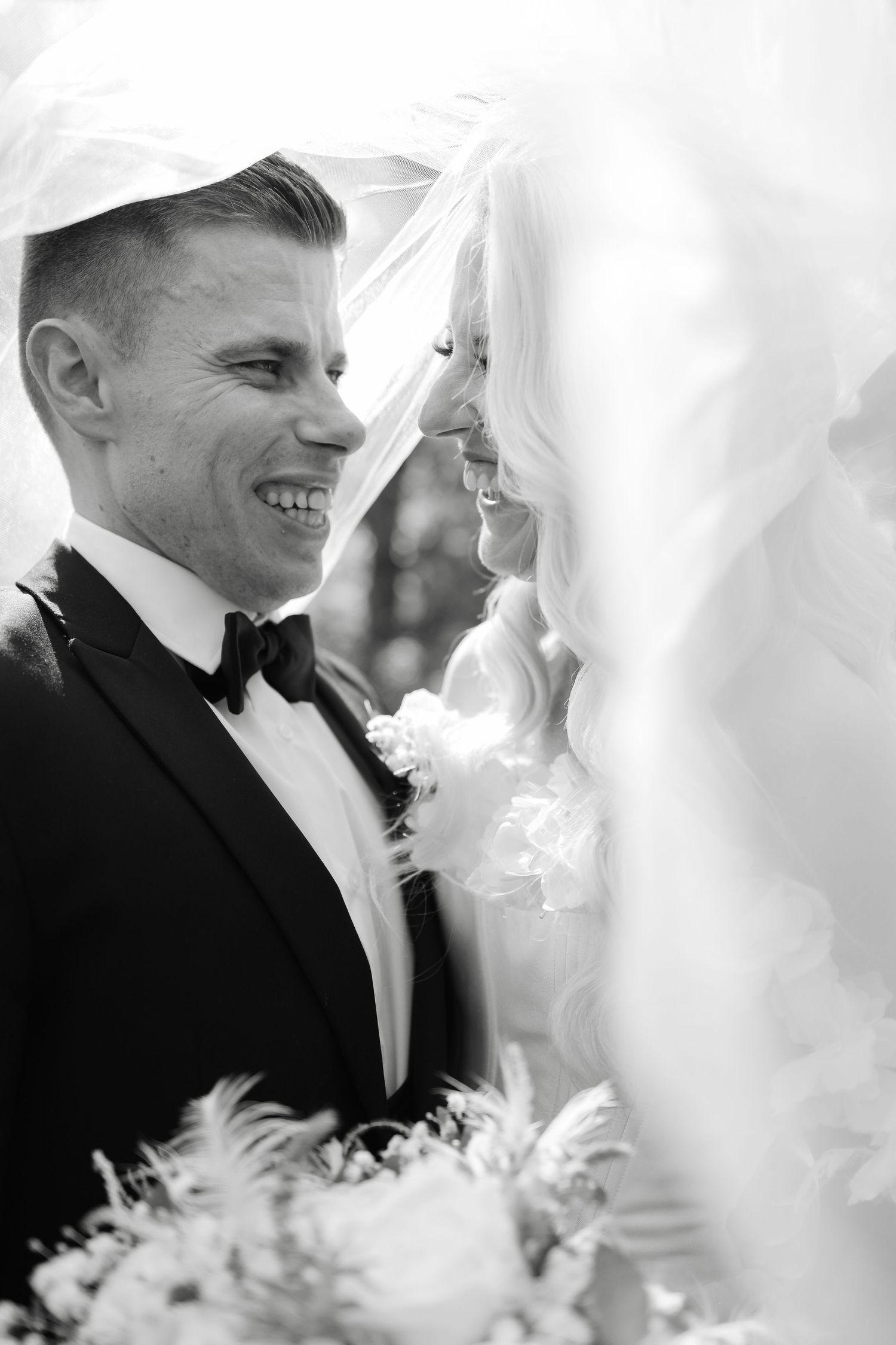 Intimate black and white wedding portrait showing tender moment between newlyweds with delicate veil and floral details.