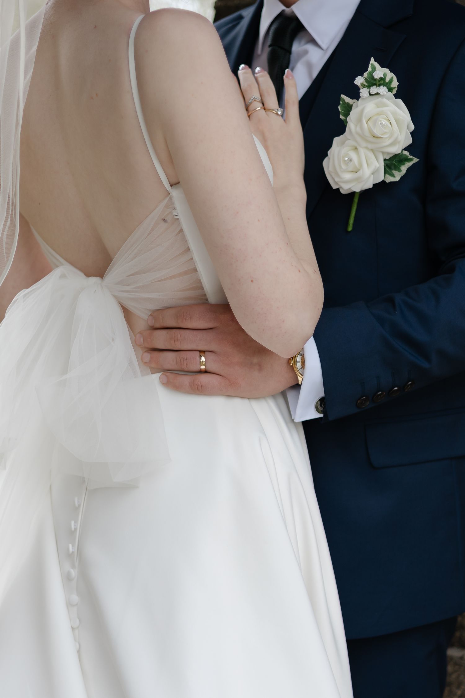 Close-up details of wedding attire showing white dress and navy suit with boutonniere.