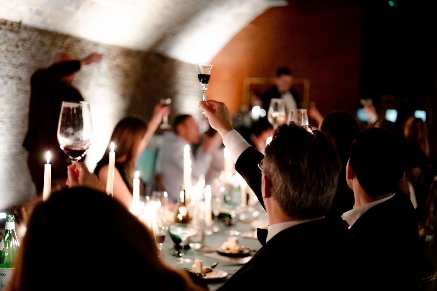 Long dining table set with glowing candles and wine glasses in a dimly lit restaurant.