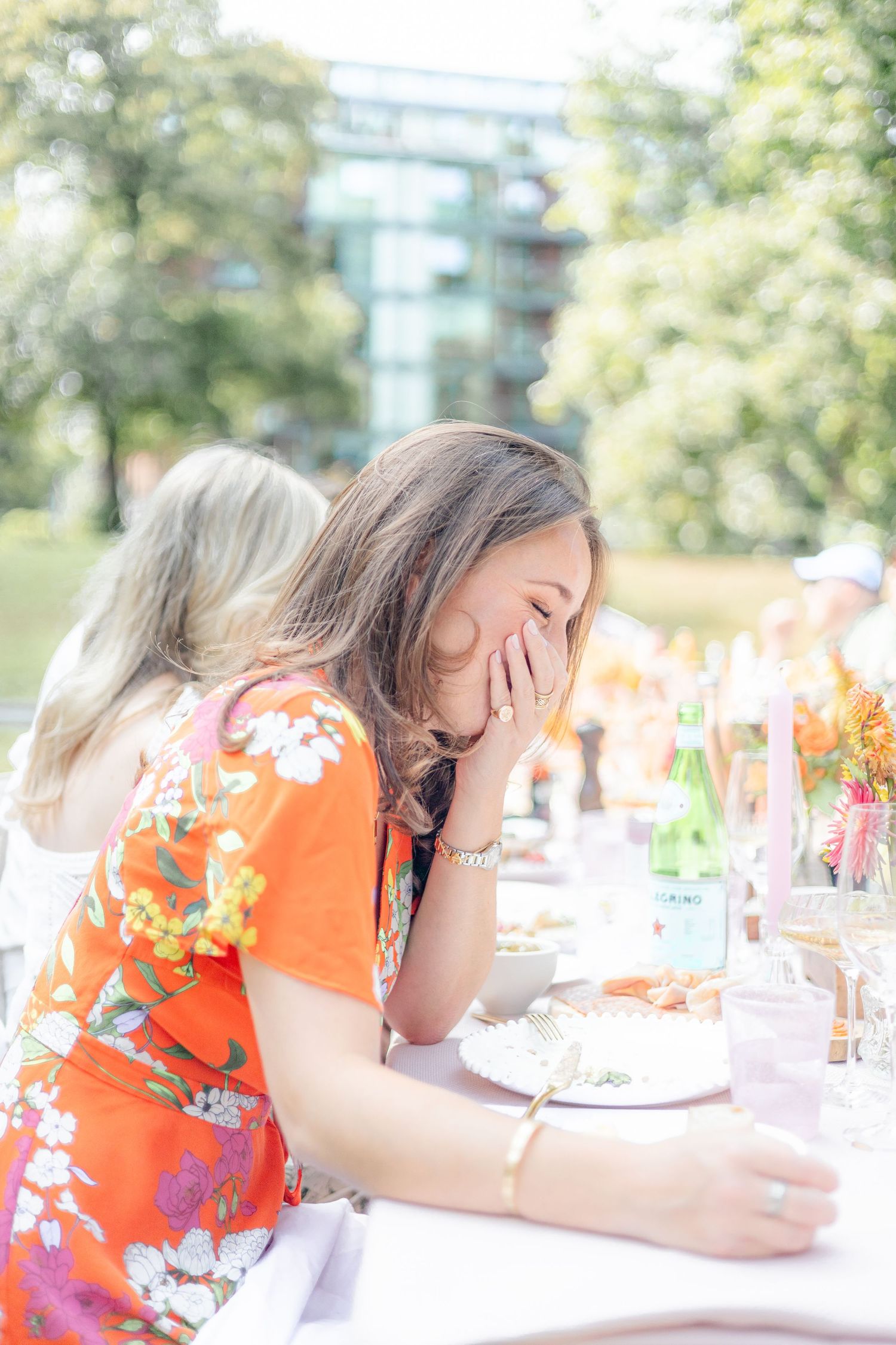 Guest in orange floral dress laughing during outdoor celebration.