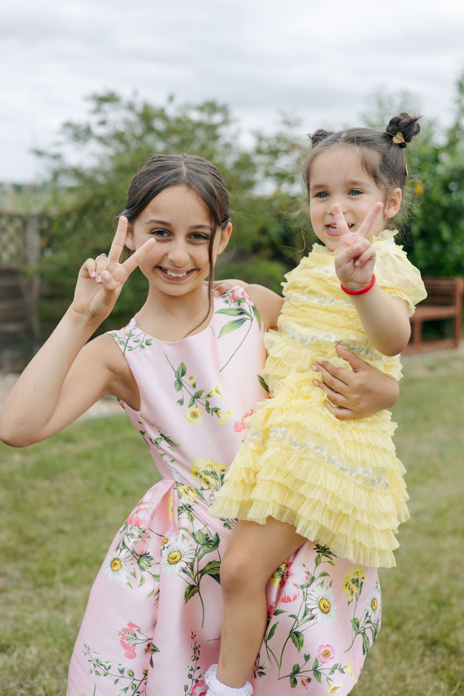Young girls in floral and yellow dresses pose playfully in an outdoor garden setting.