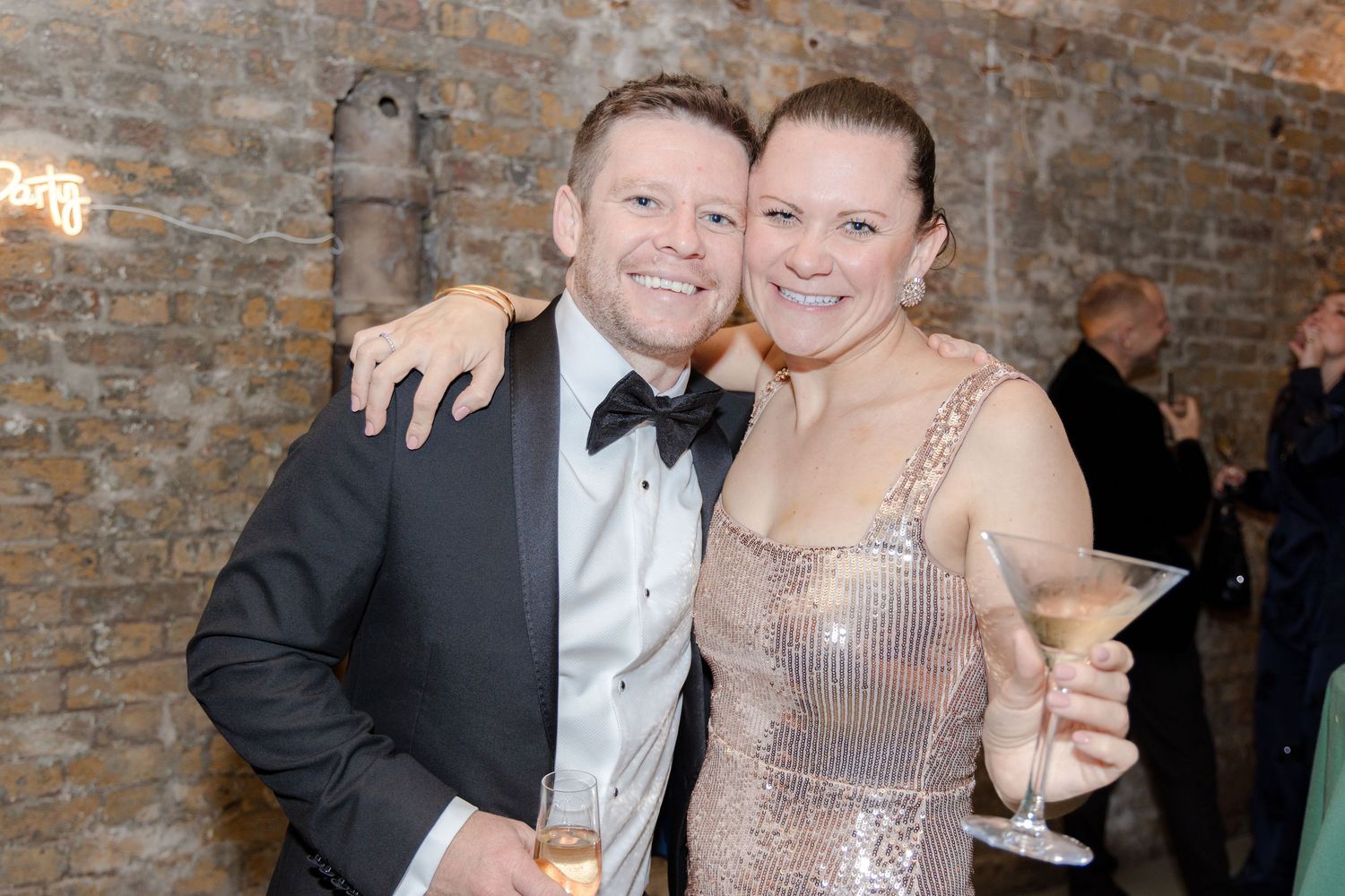 Partygoers in formal wear celebrating with champagne against exposed brick walls.