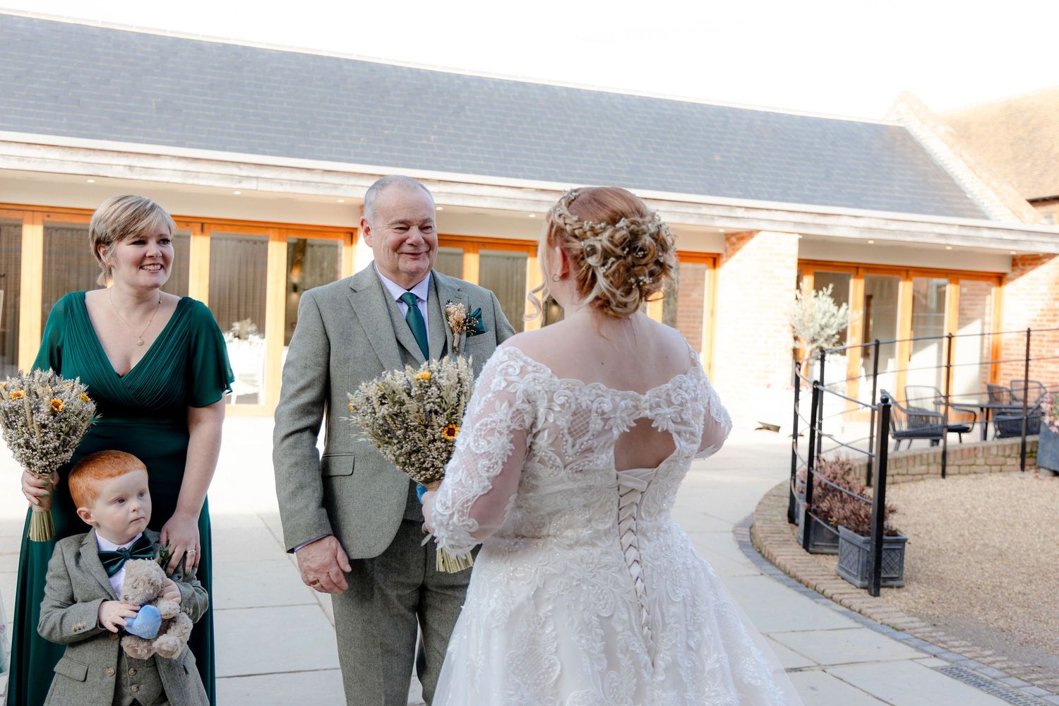 Wedding party members gather outside a venue during daytime celebrations.
