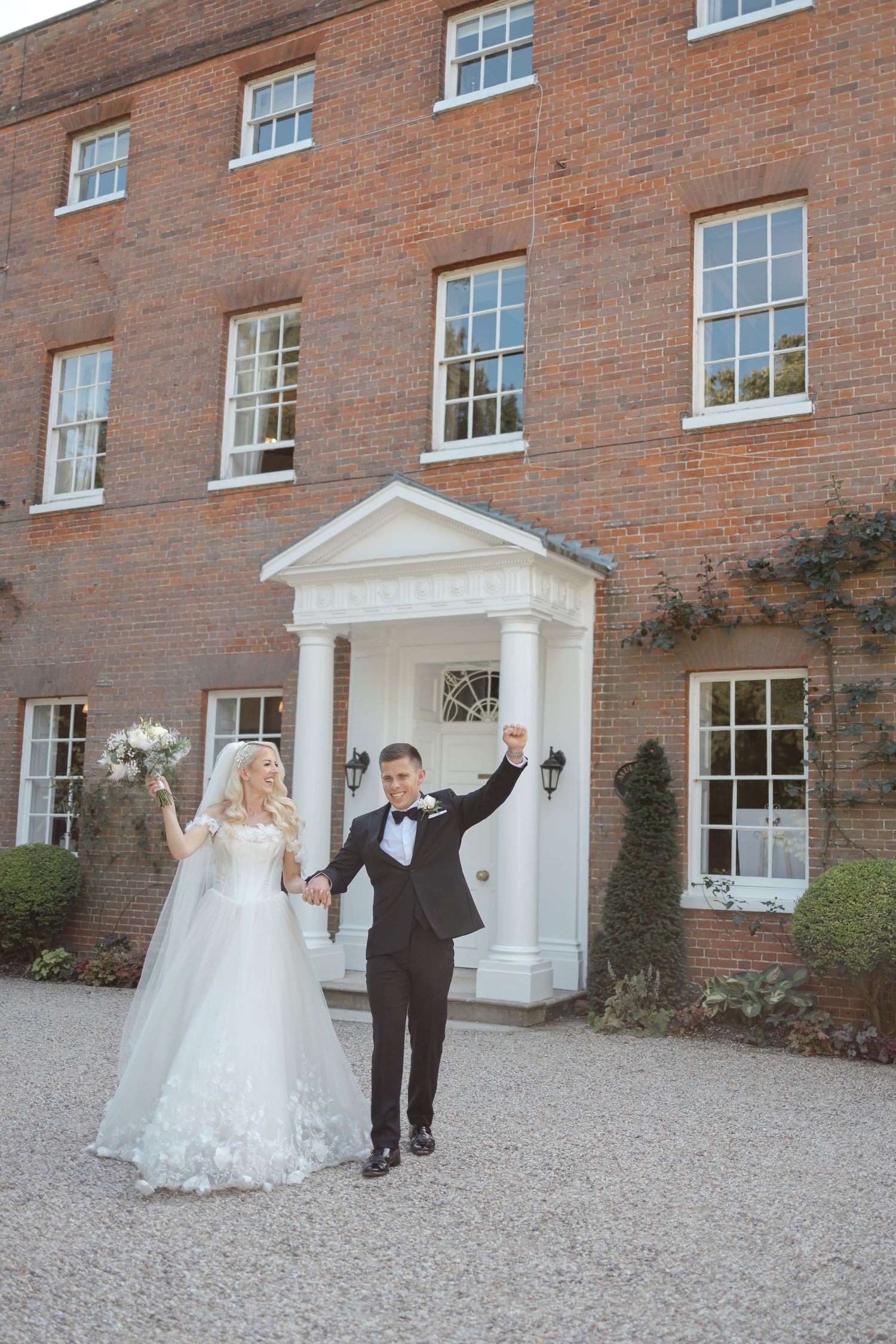 Wedding couple celebrates outside a grand Georgian brick building with white doorway.