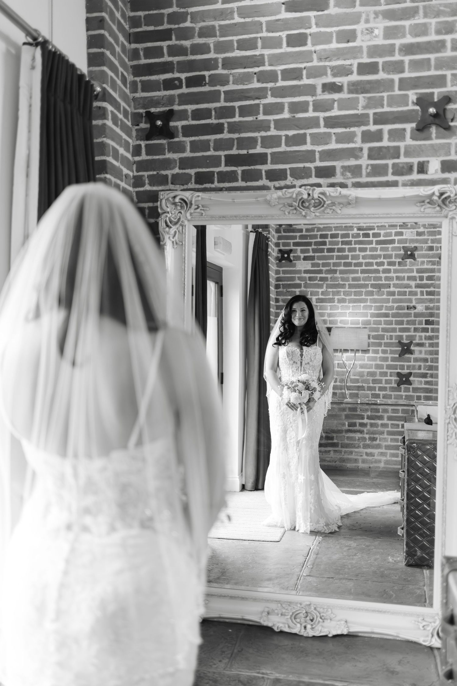 A white wedding dress and veil displayed in front of exposed brick walls with natural lighting.