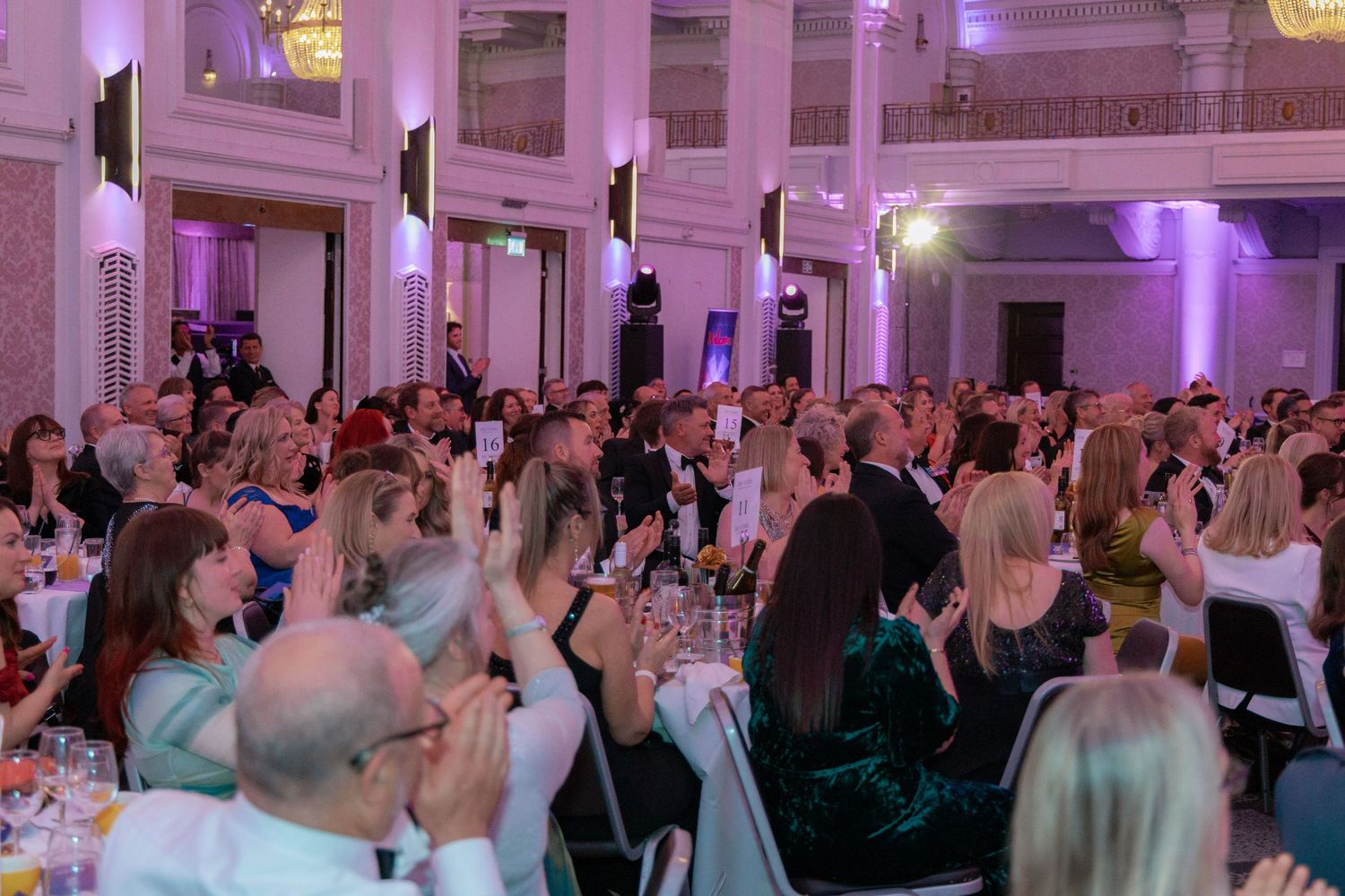 Large crowd of guests celebrating at an indoor event with purple ambient lighting.