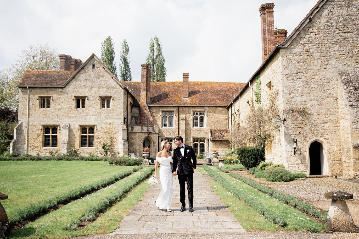 Newlyweds walking down a garden path at an elegant stone country estate.