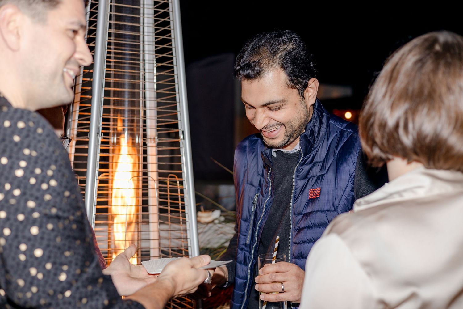 People socializing near an outdoor patio heater at night during a gathering.