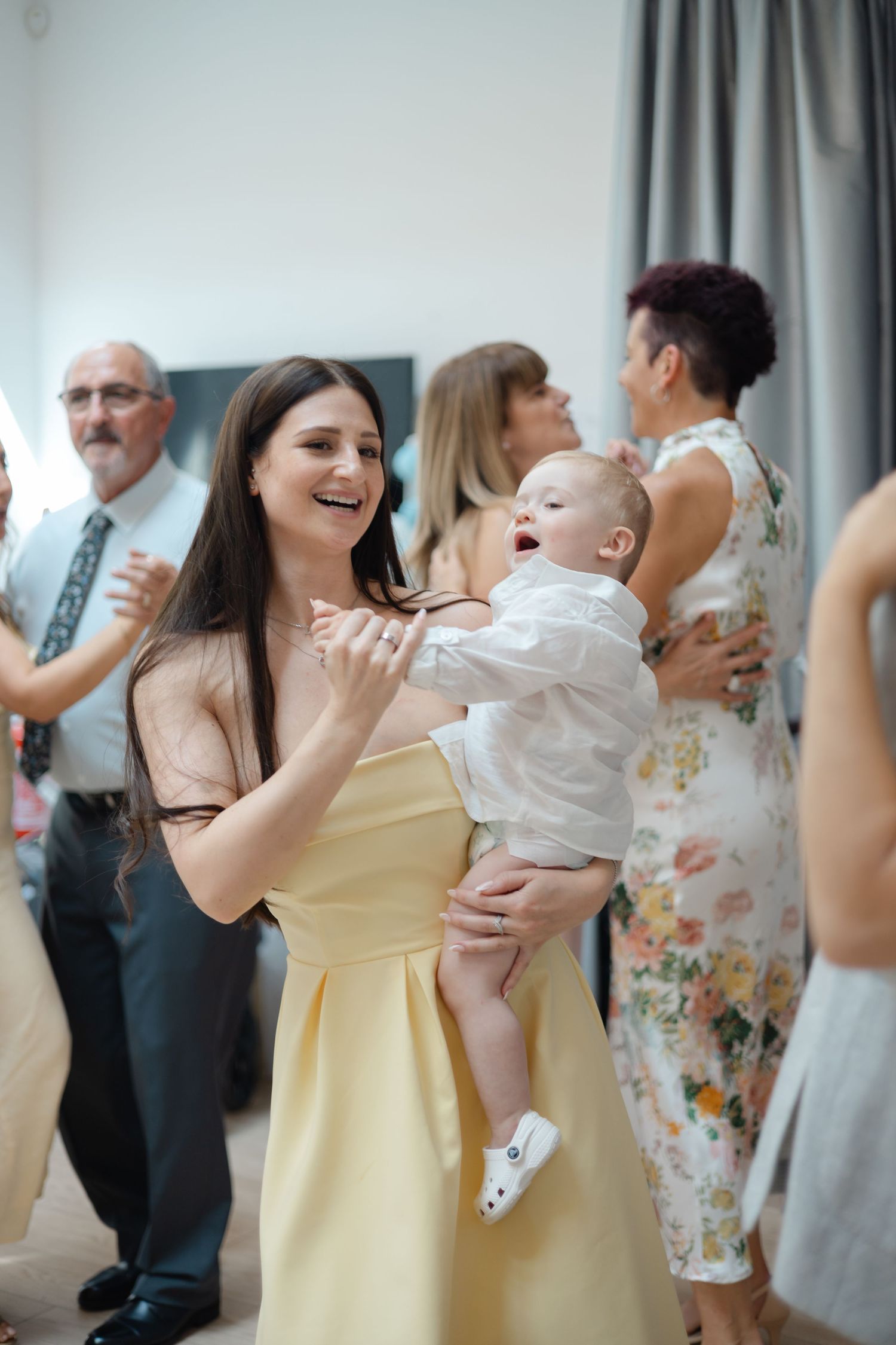 People dancing and celebrating at a party with blue curtains and festive atmosphere.