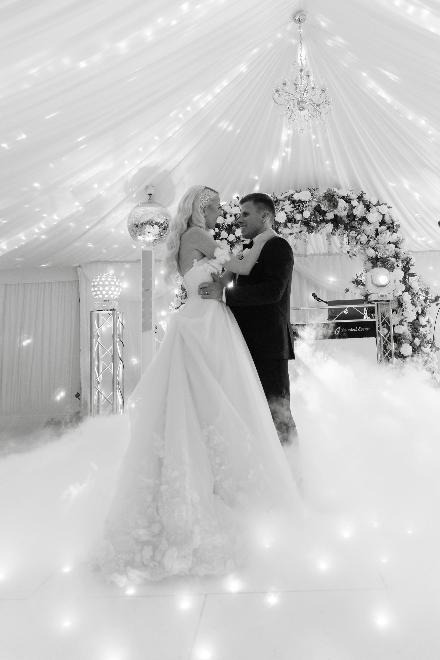 Dreamy wedding reception scene with white draping, chandeliers and dancing in ethereal lighting.