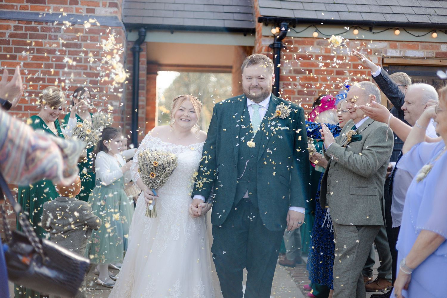 Joyful wedding celebration with confetti toss outside historic brick venue.