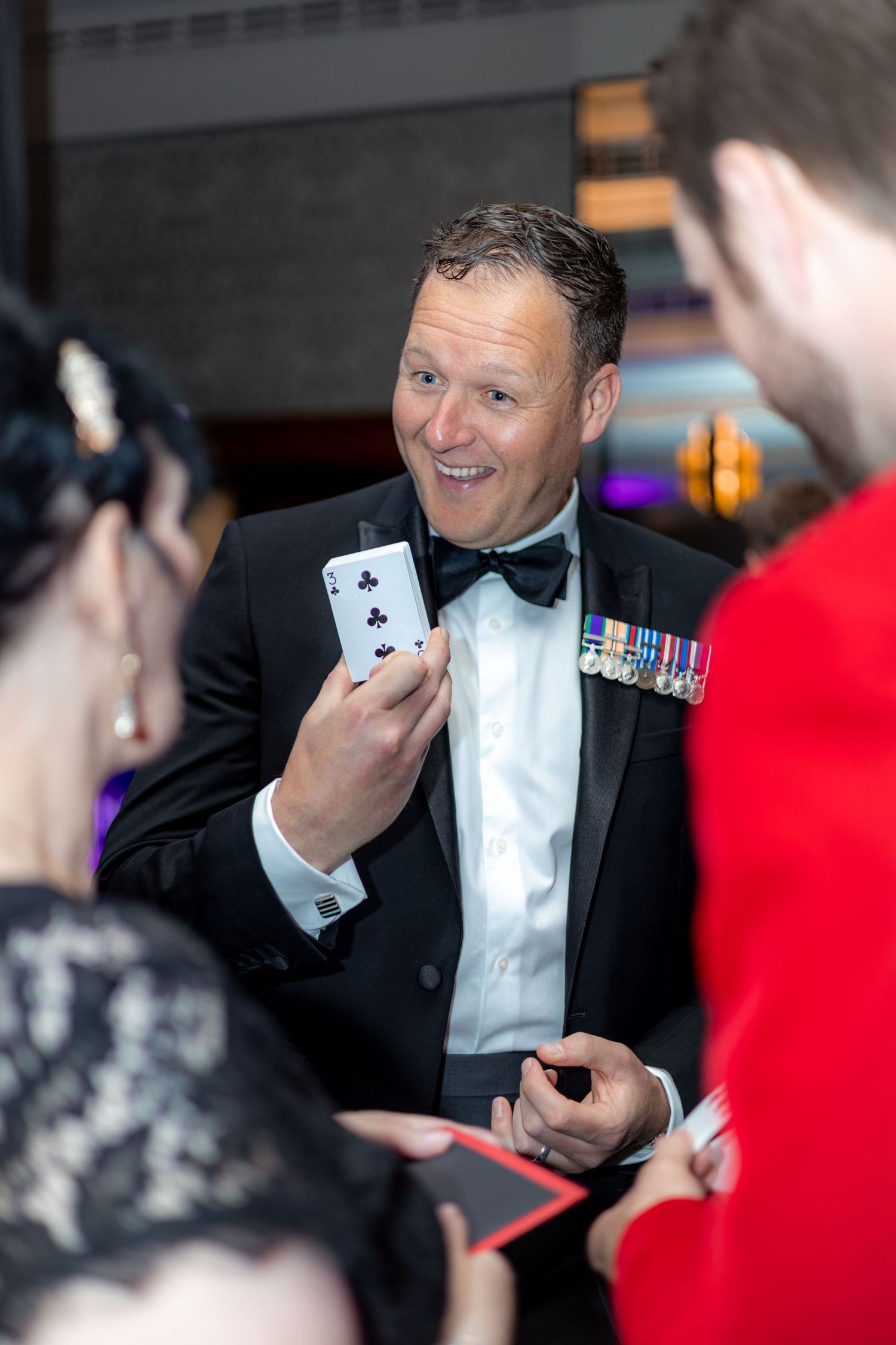 A performer shows playing card magic tricks to an audience at a formal event.