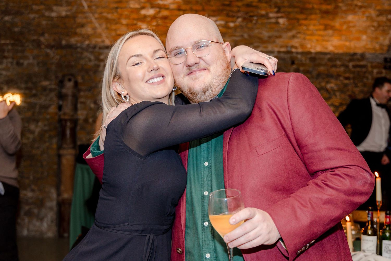 Celebratory group sharing joyful moments at a formal event against rustic brick walls.