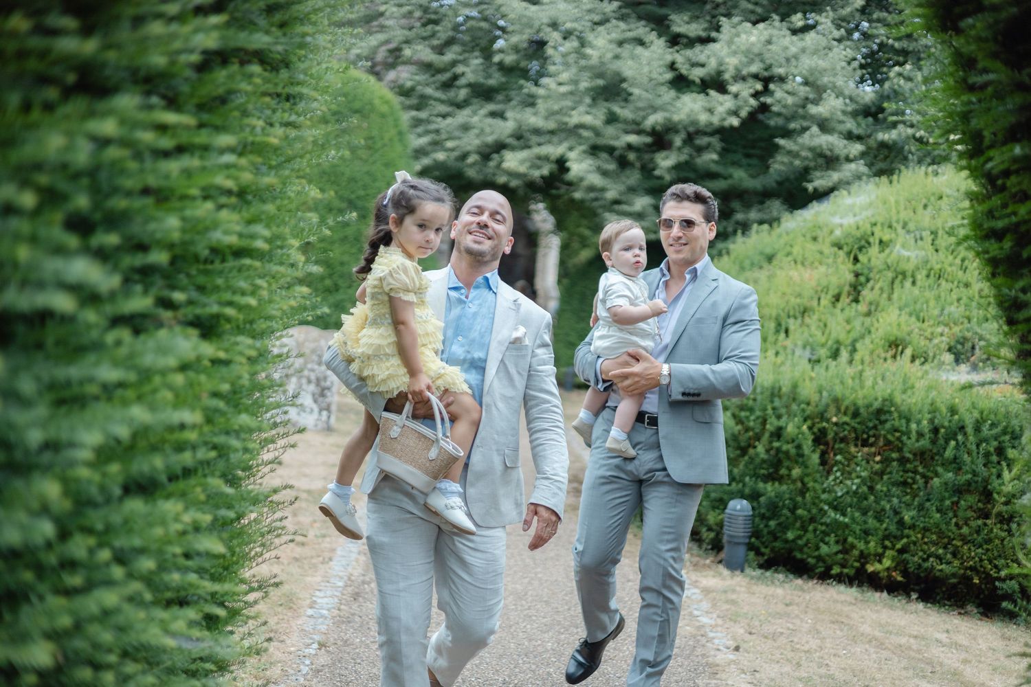Family members in gray suits walk together on a garden path surrounded by lush greenery.