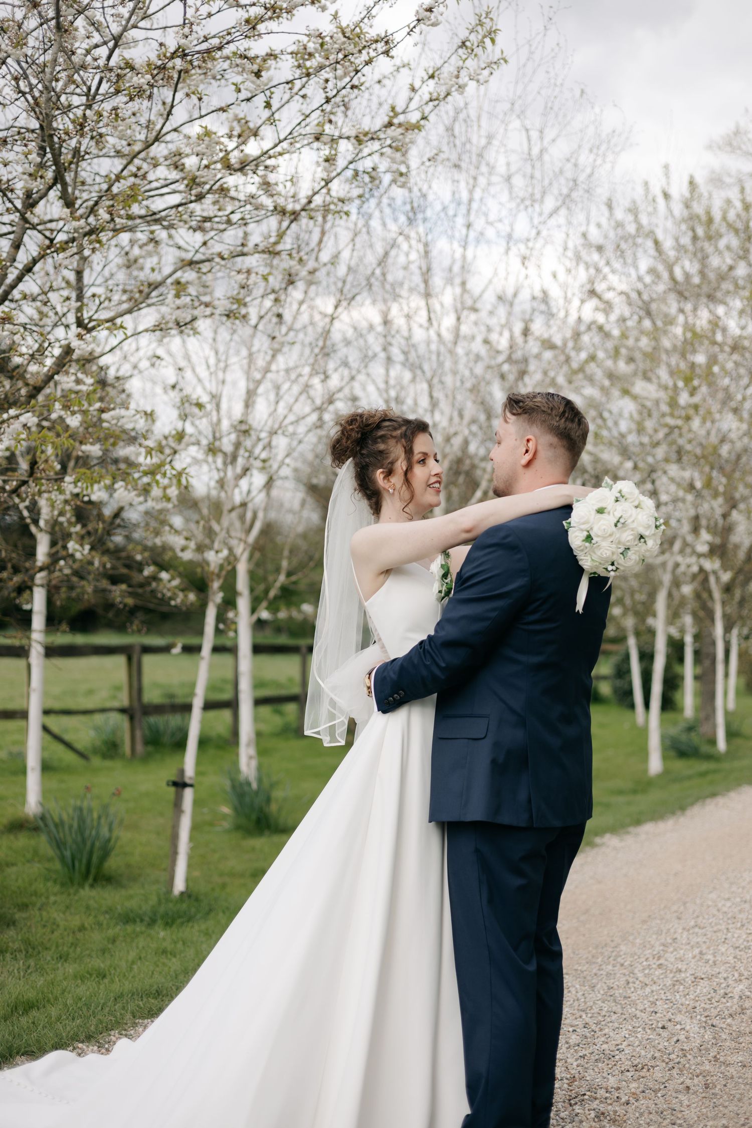 Couple embraces on a tree-lined path surrounded by white birch trees in spring.