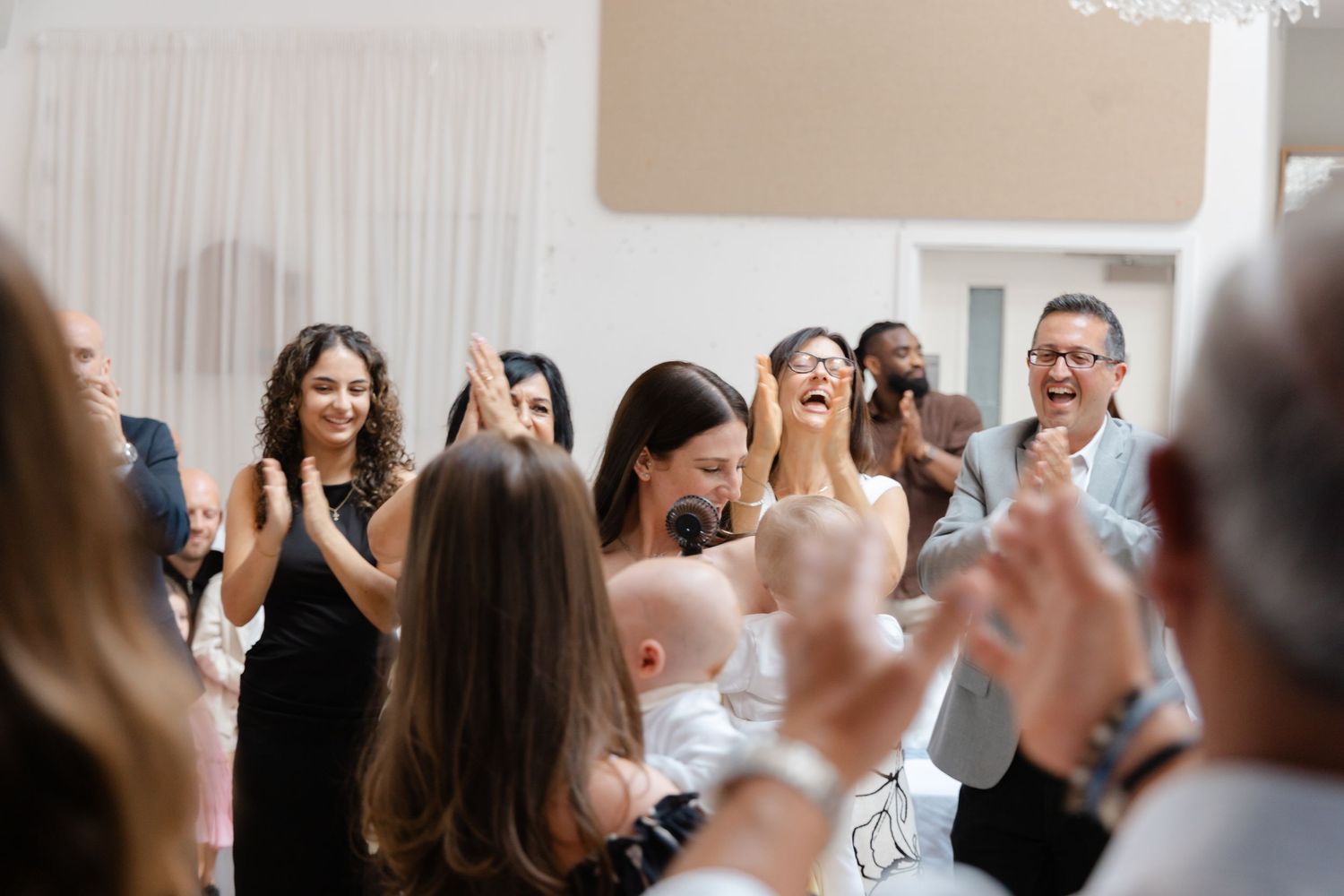 Joyful celebration with guests laughing and dancing in a white-draped event space.
