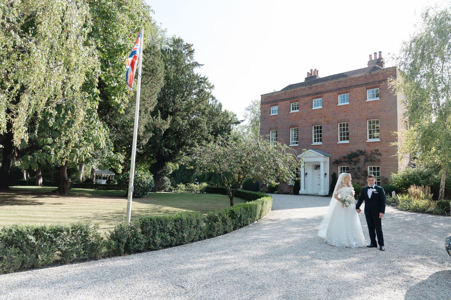Wedding couple walking along gravel path at elegant country estate with Union Jack flag.