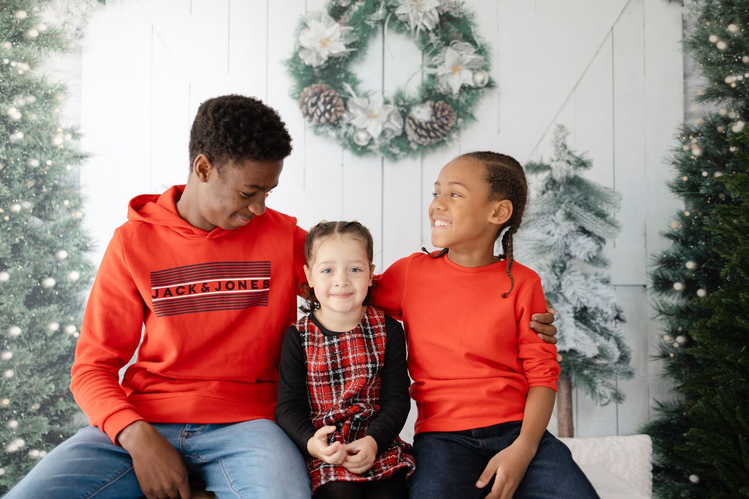A festive family portrait with matching red outfits against a winter backdrop with wreaths and trees.