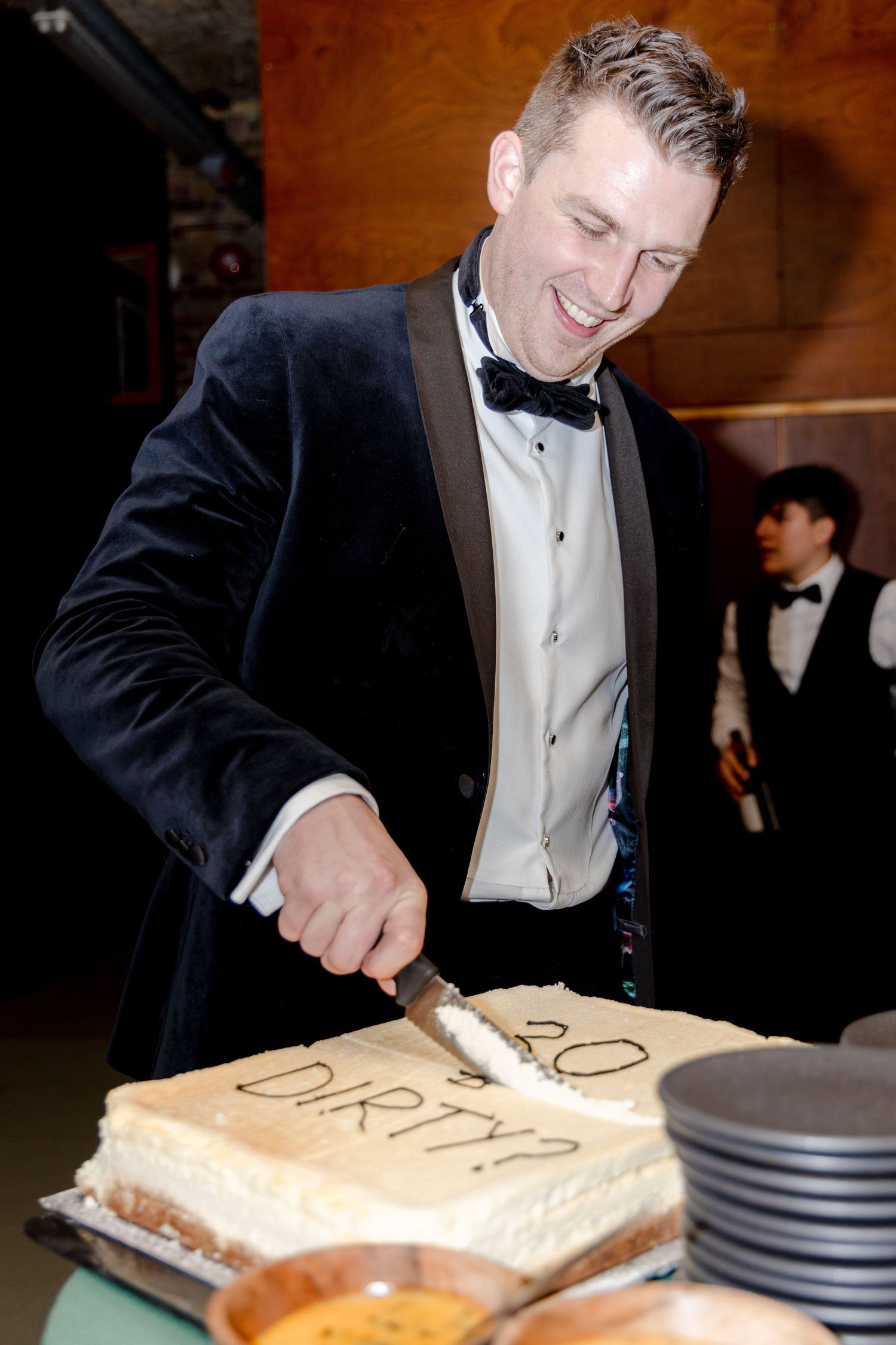 Person in tuxedo cutting a decorated cake at formal event.