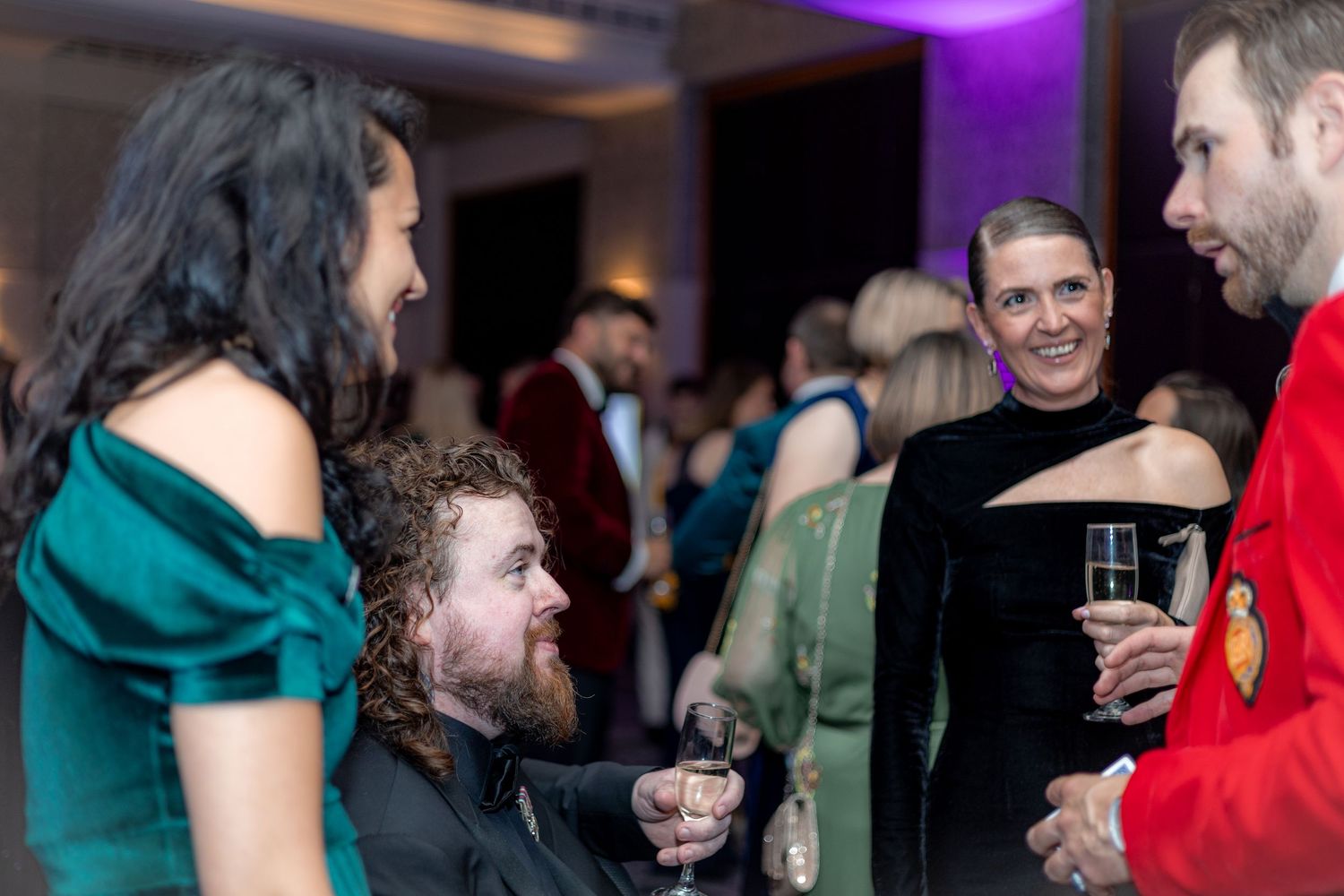 Guests mingle and socialize at an evening party with purple ambient lighting.