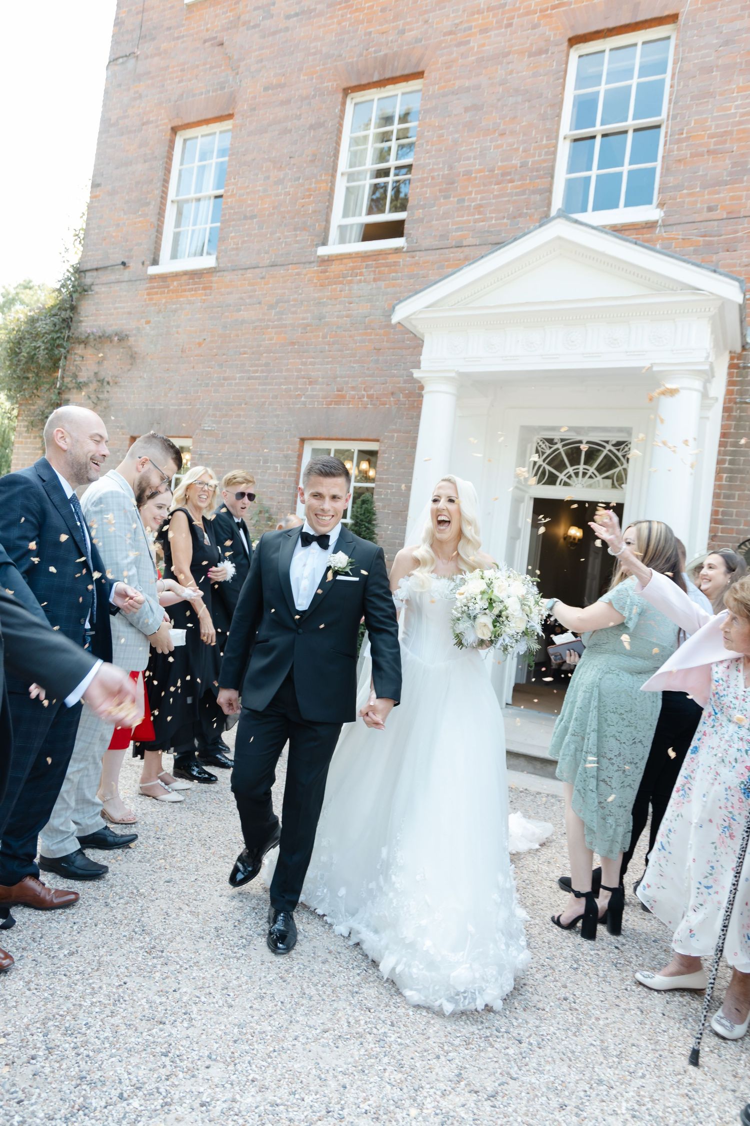 Newlyweds exit historic venue while guests shower them with confetti.