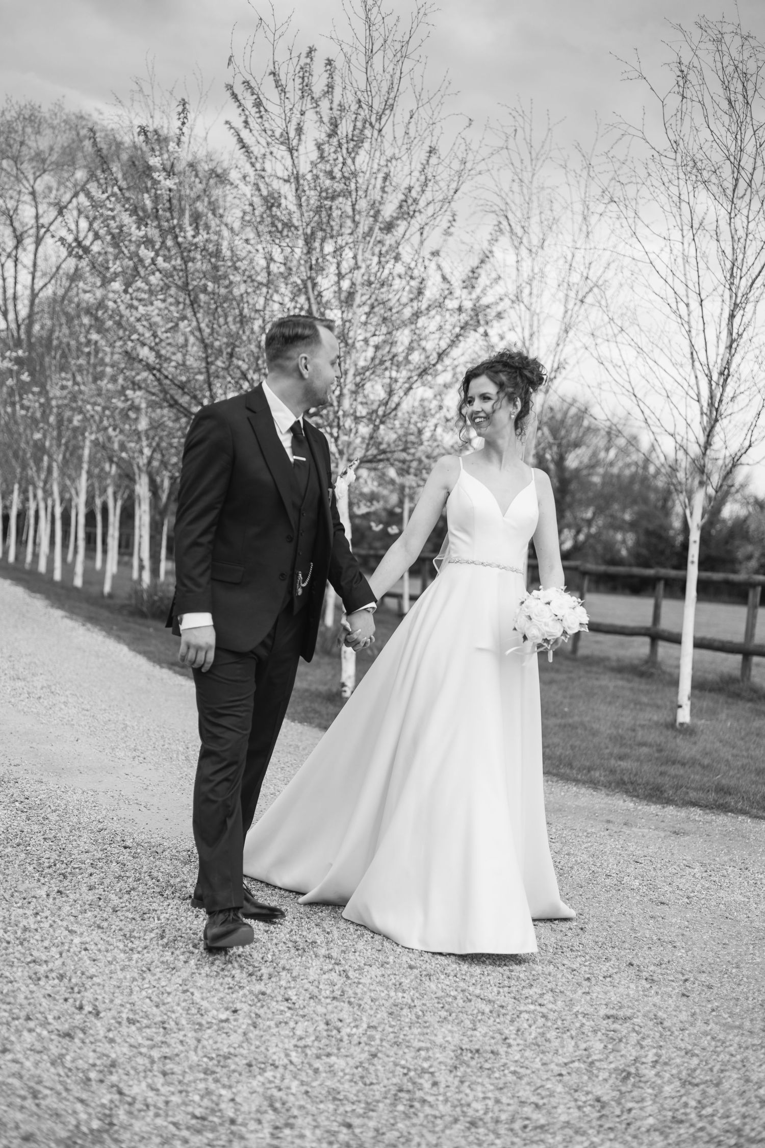 Black and white series of newlyweds walking and dancing on gravel path between birch trees.