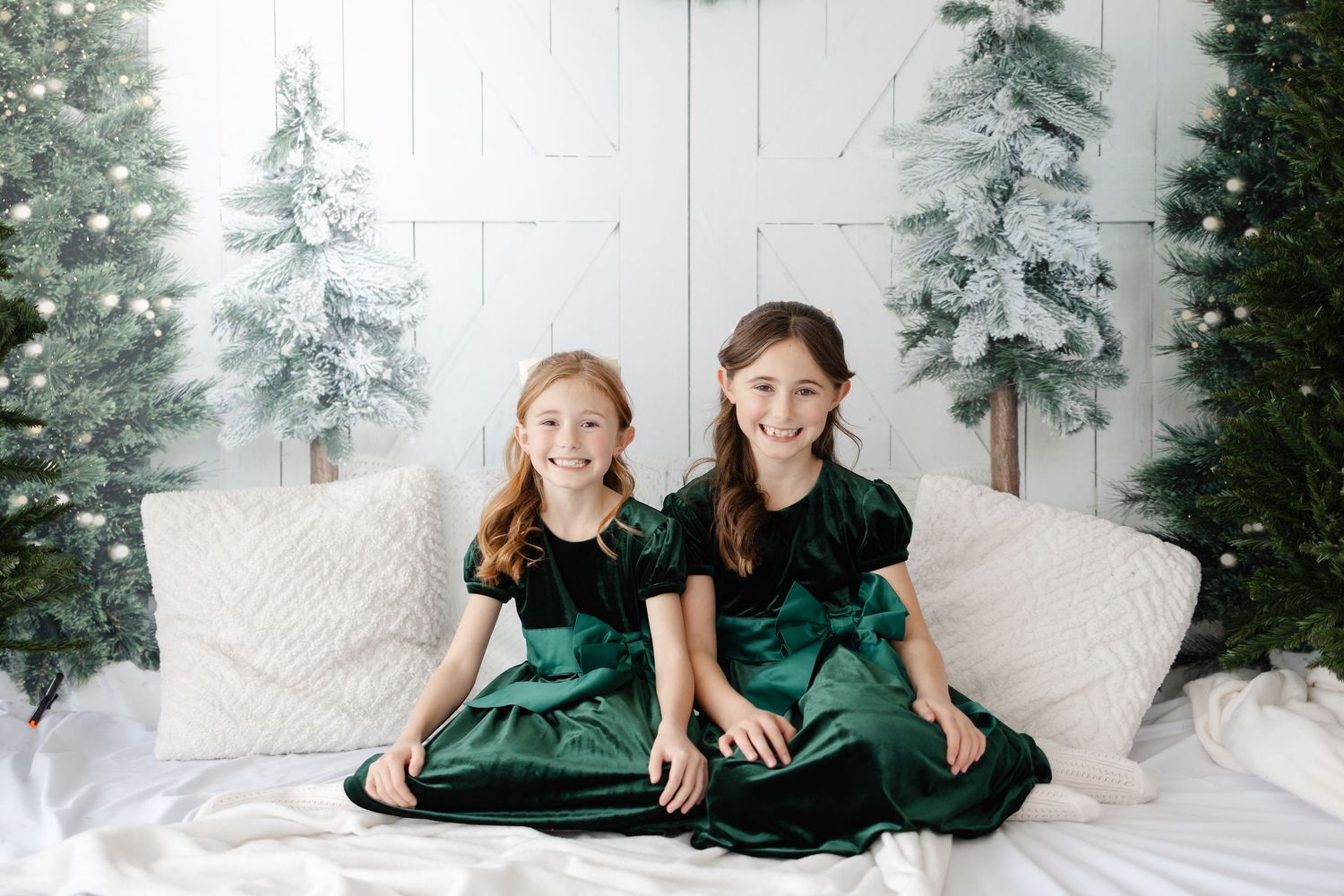 Family members in coordinating dark outfits pose against winter-themed backdrop with evergreen trees.