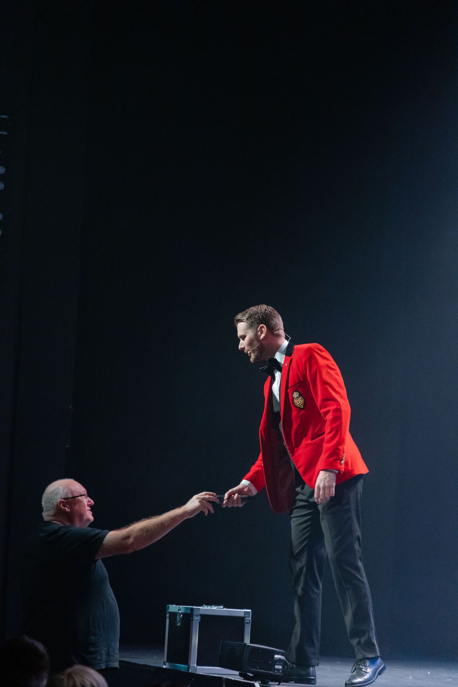 Performer in red jacket on dark stage during theatrical performance.
