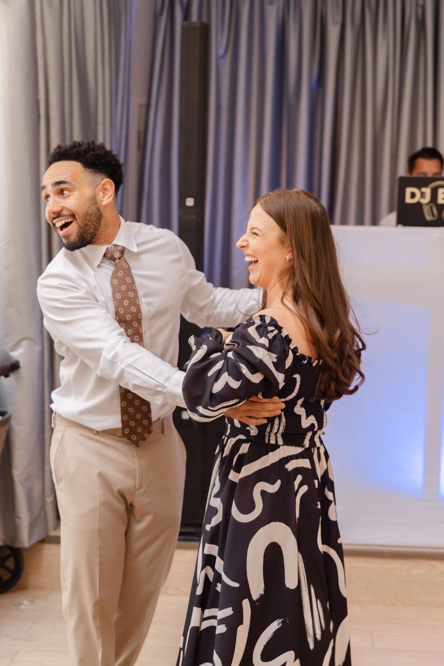 Two guests laughing while dancing together at an indoor event.