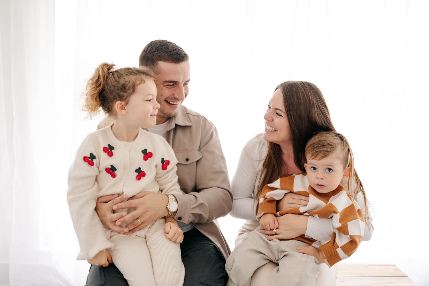 A family sitting together on a couch wearing coordinated neutral-toned outfits.
