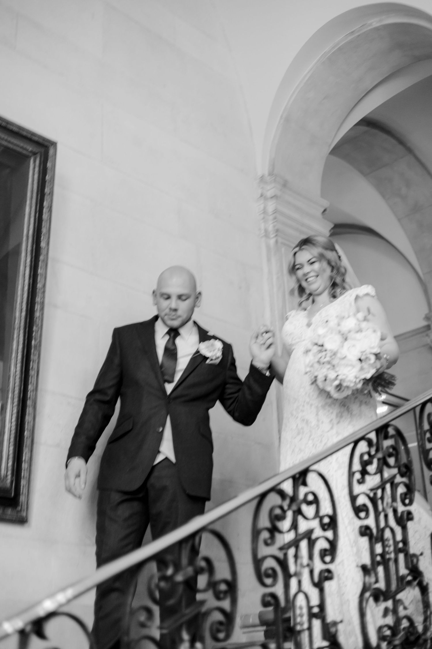 Couple shares a joyful moment on an elegant staircase with decorative iron railings.