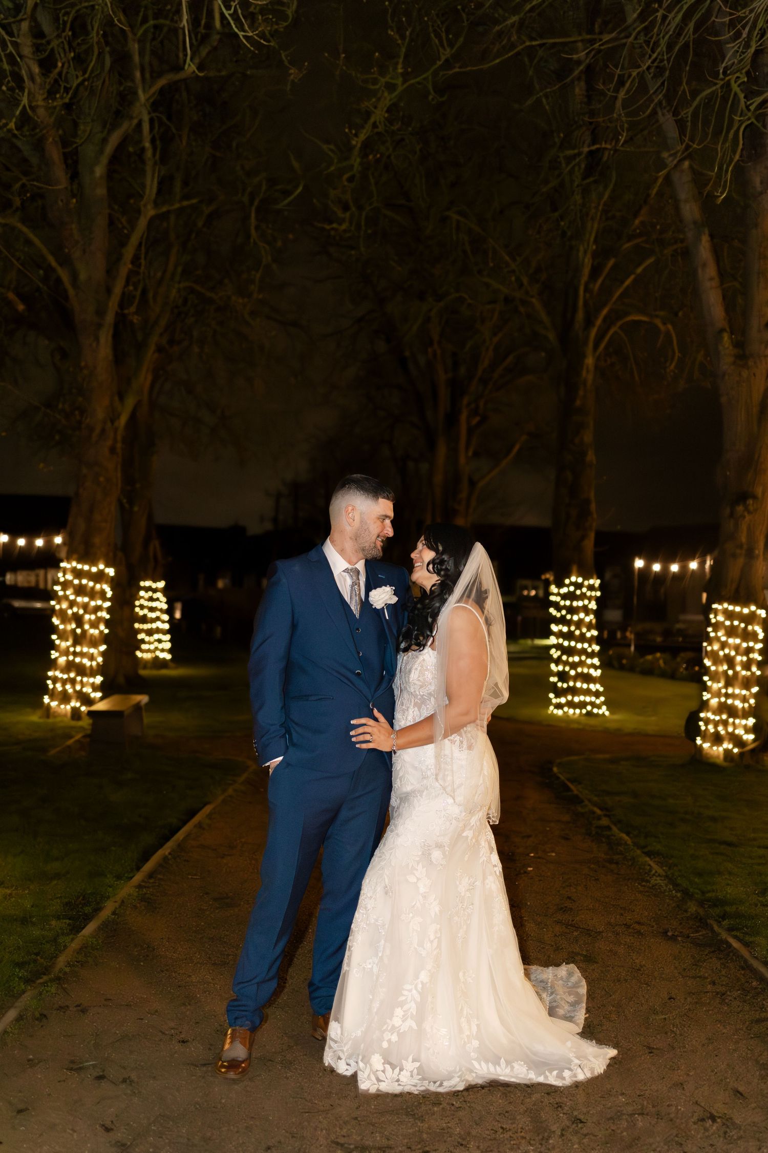 Evening wedding photos with trees decorated in warm string lights creating a romantic atmosphere.