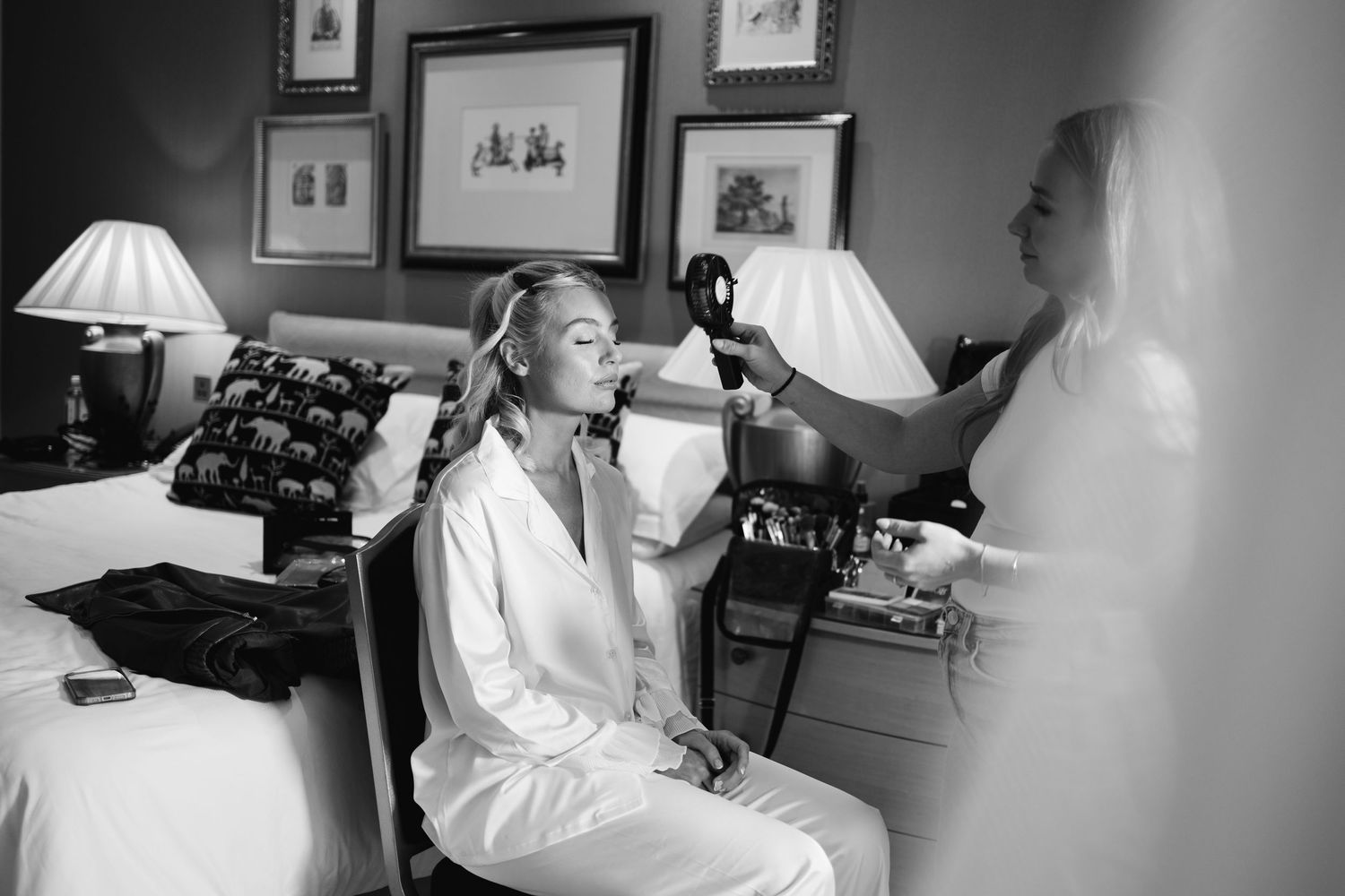 Black and white photo of wedding morning preparations in a room with framed artwork.