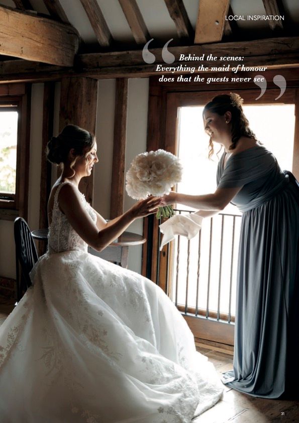 Candid moment between a bride in white gown and someone in blue passing a bouquet in rustic setting.